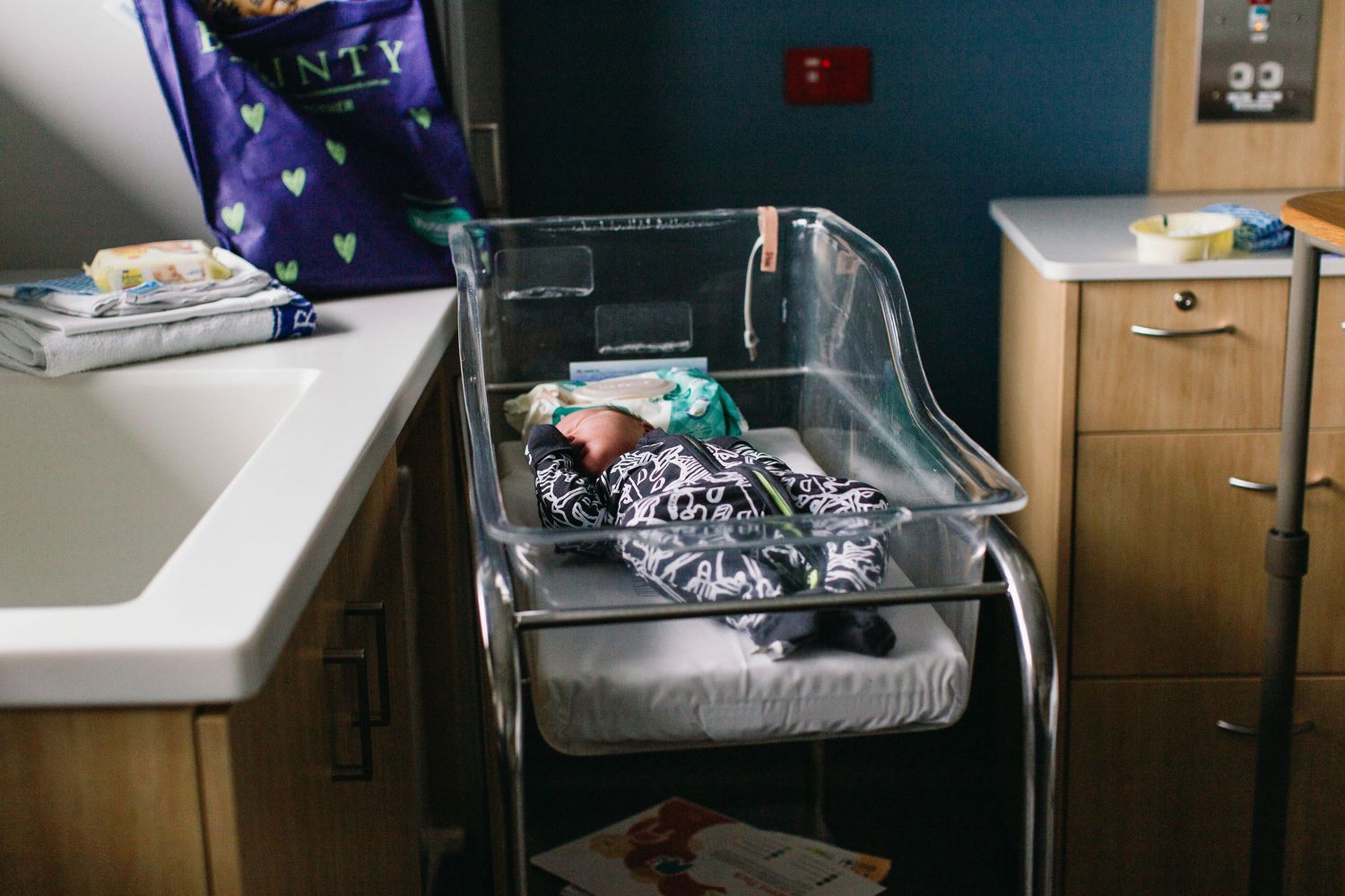 Newborn baby sleeping peacefully in a hospital bassinet in a maternity ward room.