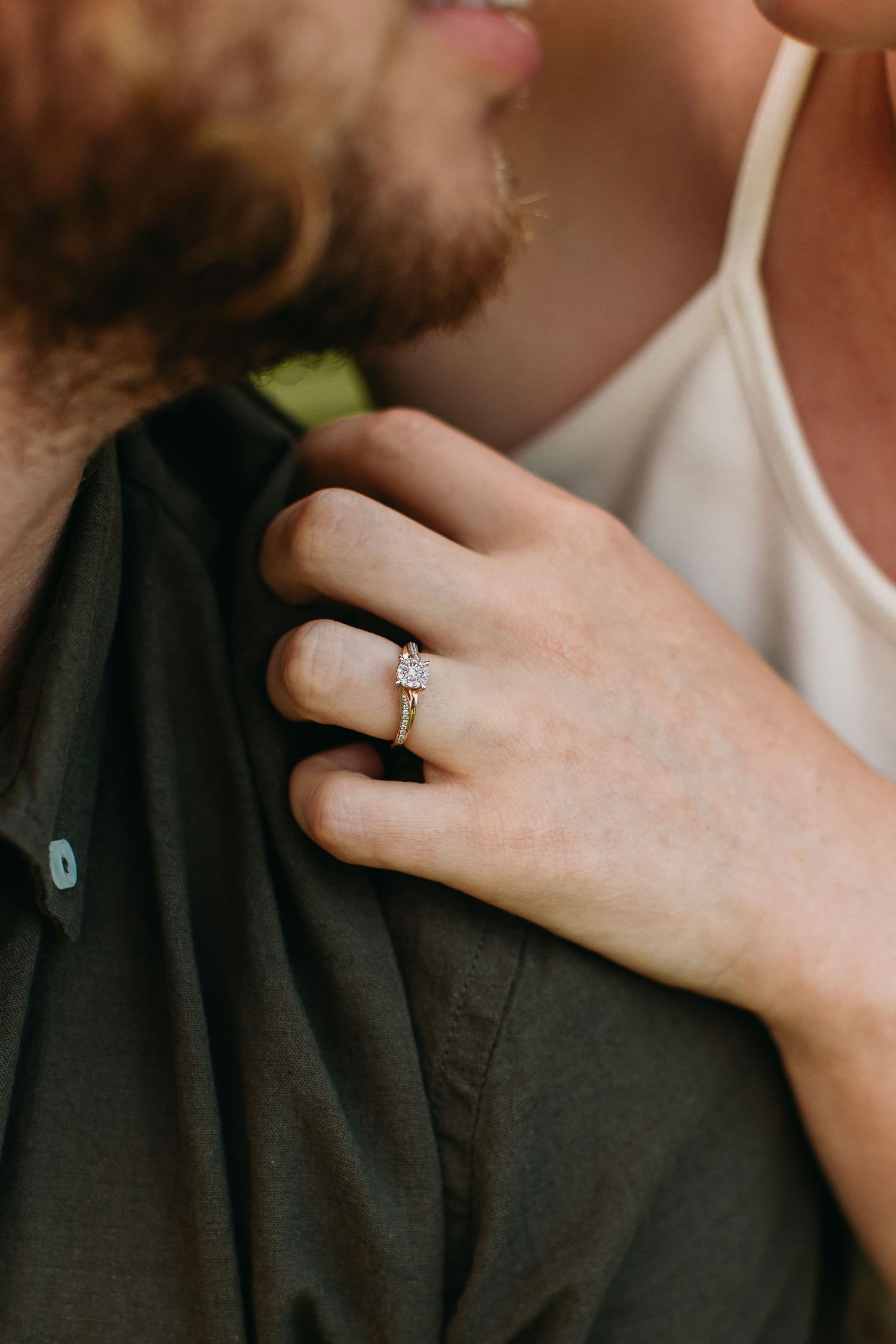 Close-up of a woman's hand with a diamond engagement ring resting on a man's dark shirt.