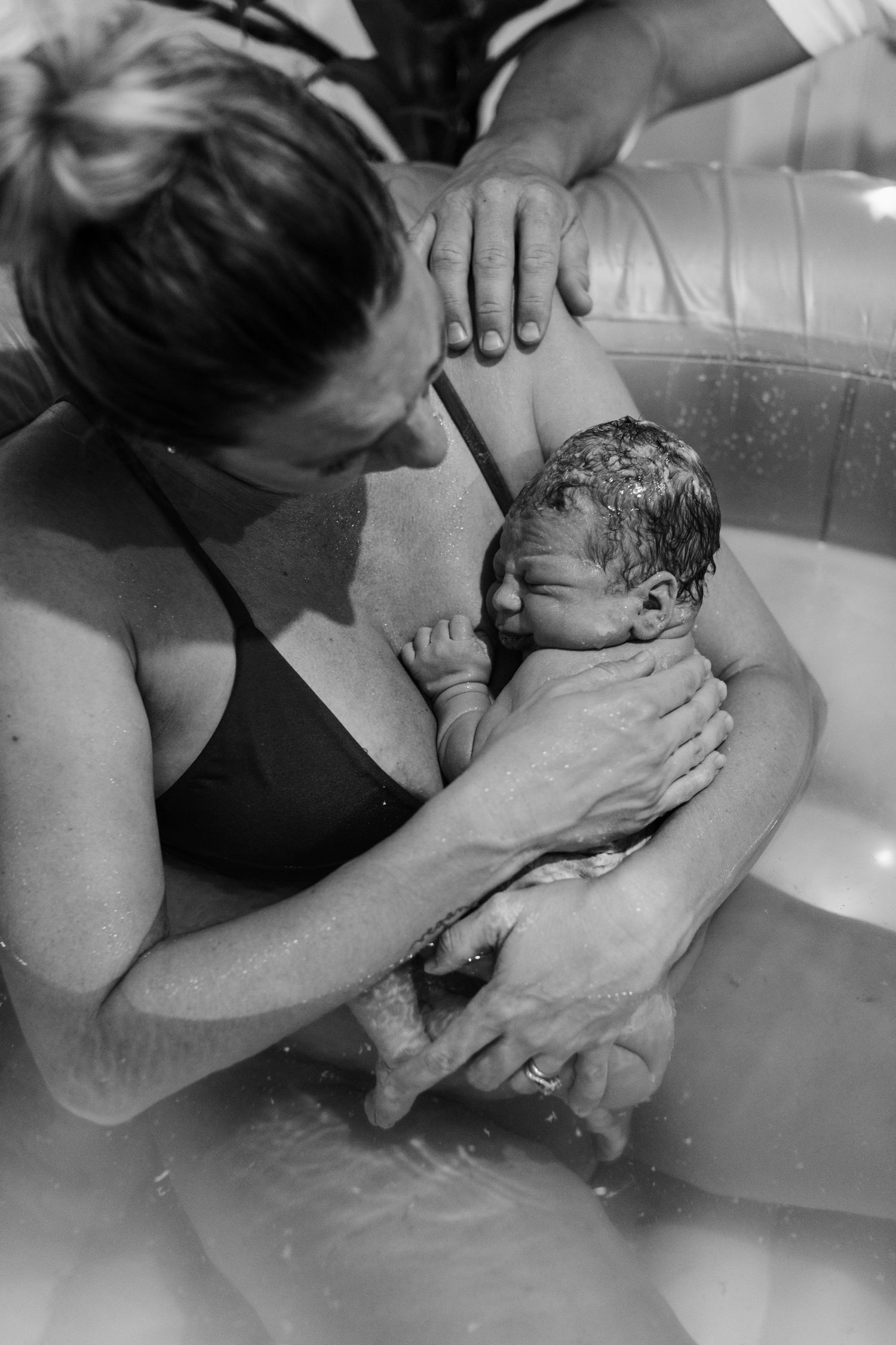 Black and white photo of a mother holding her newborn baby during a water birth in an inflatable pool.