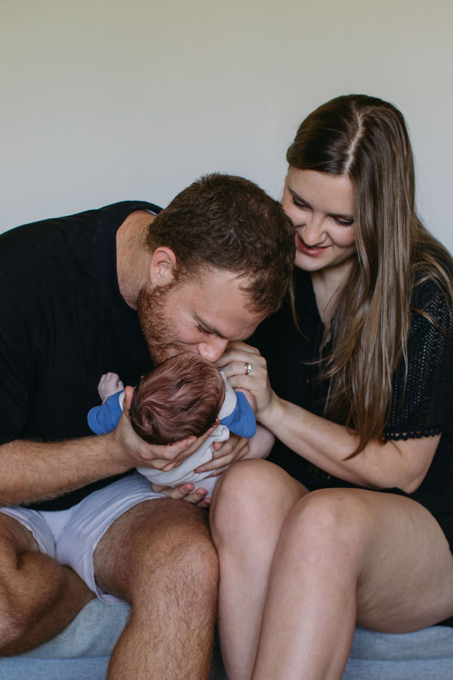 Parents lovingly kiss and cuddle their newborn baby together, sharing a tender family moment.