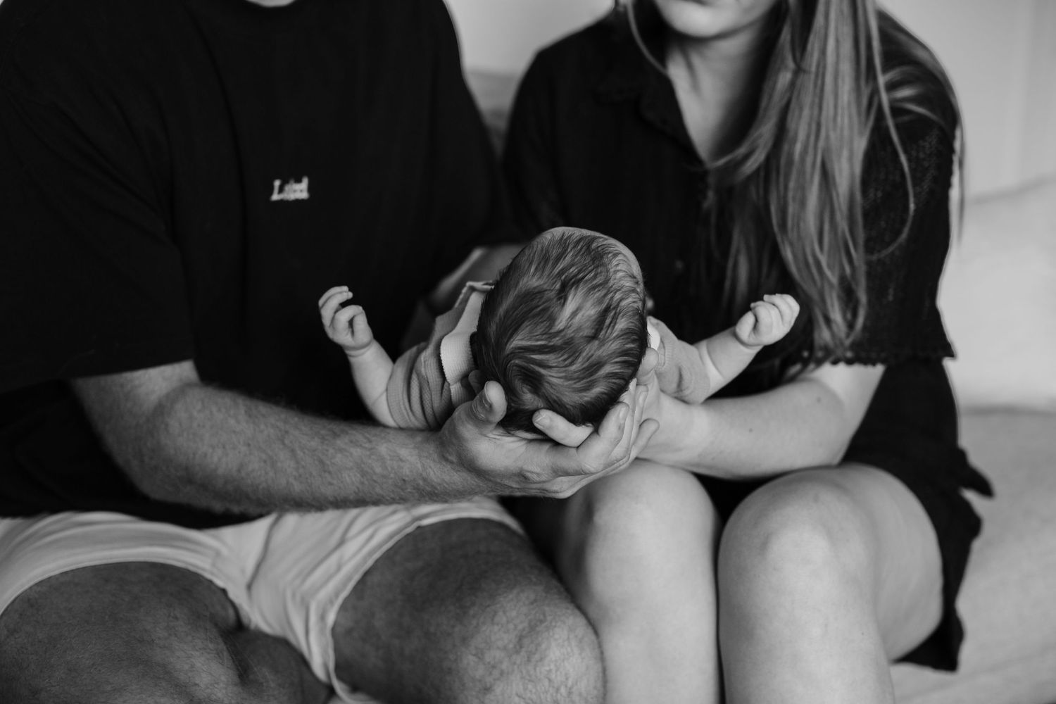 Parents holding their newborn baby together in a tender black and white portrait photo.