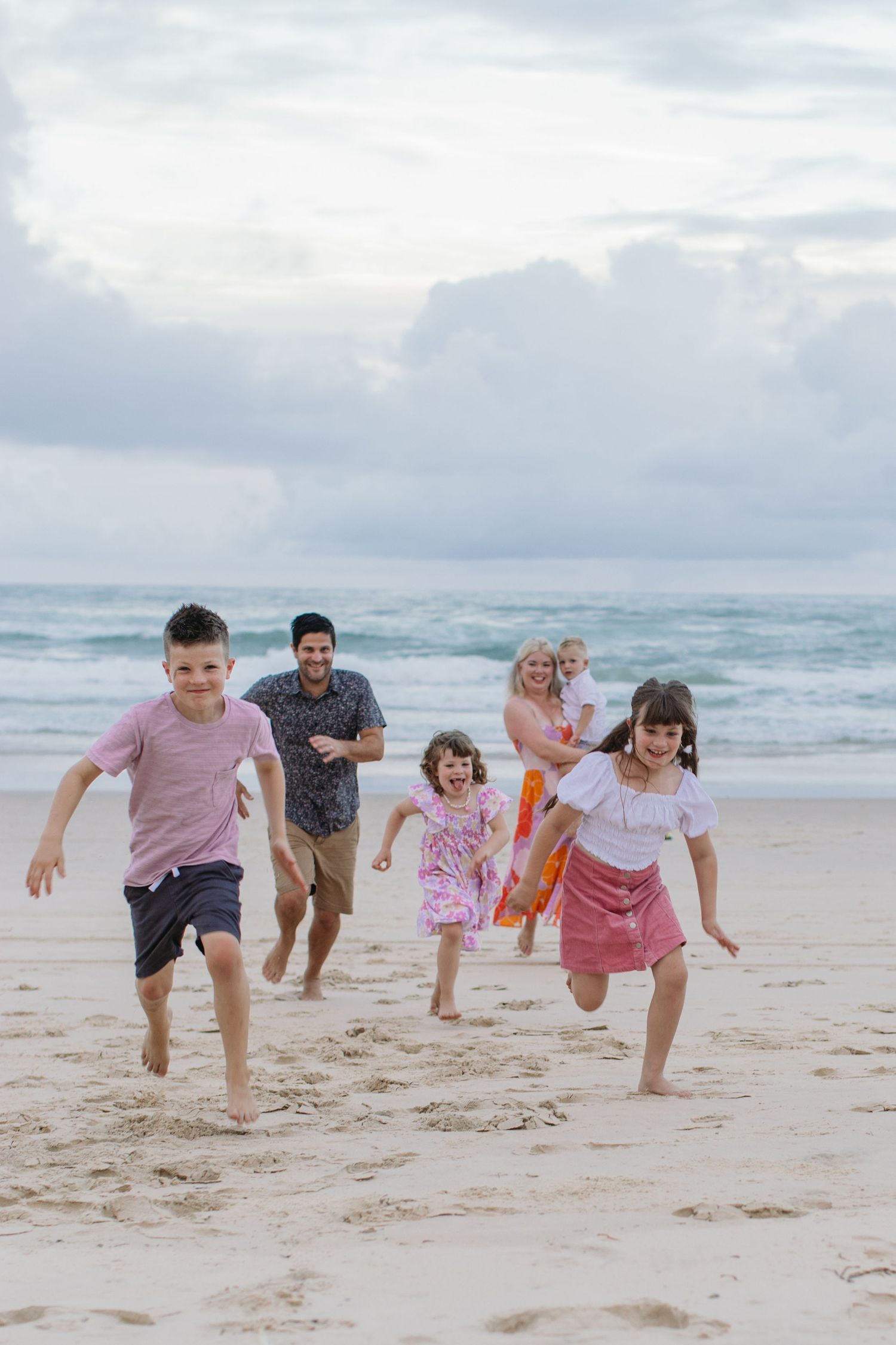 Joyful family with three children running on a sandy beach with ocean waves.