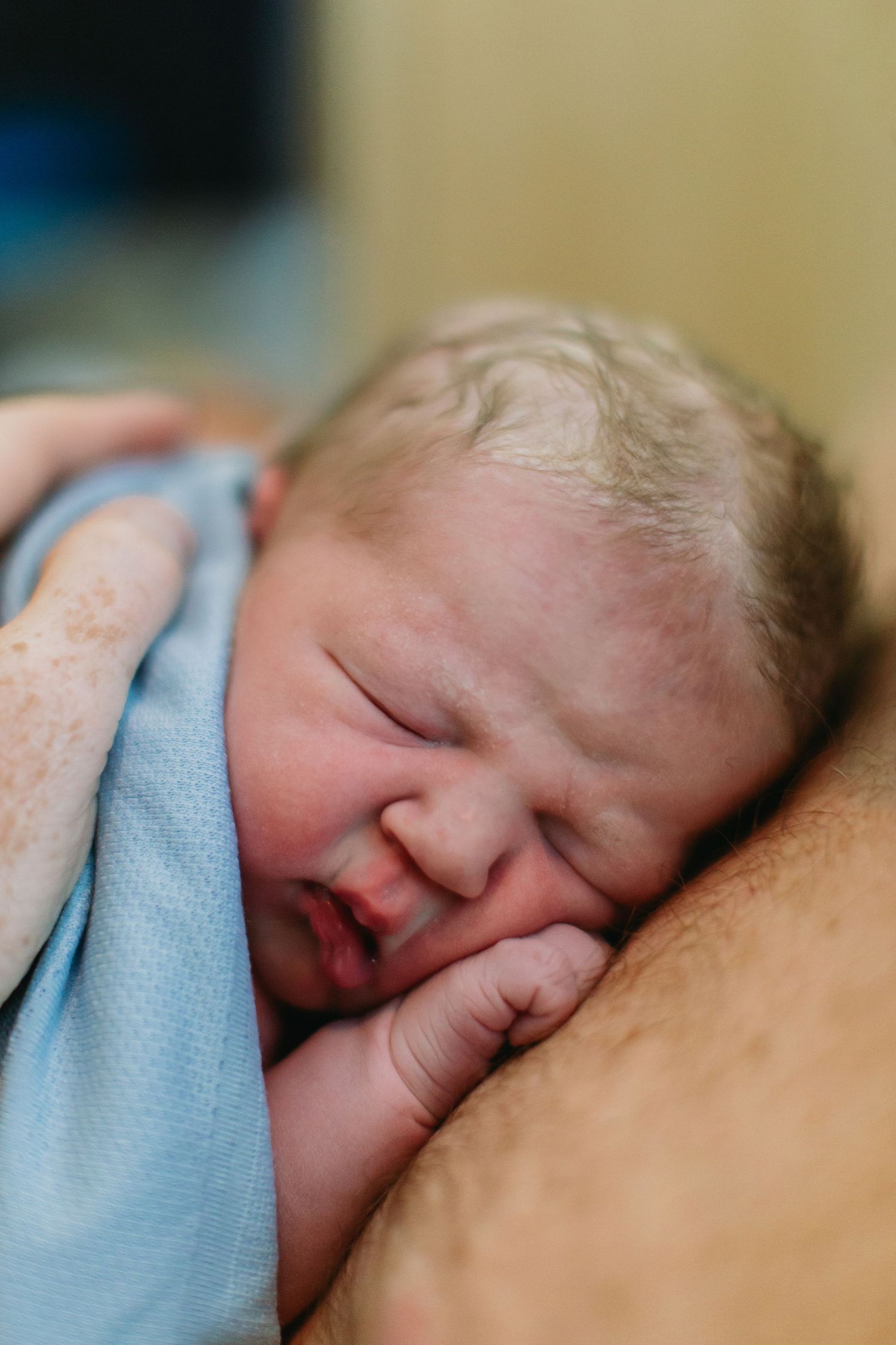 Close-up of a peaceful newborn baby with light hair sleeping wrapped in a soft blue blanket.