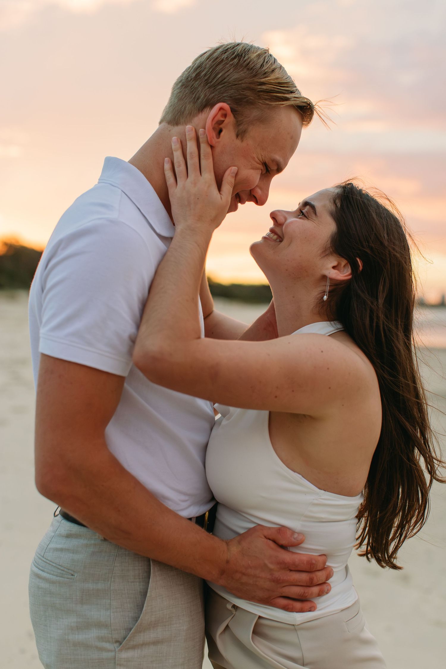 Romantic couple embracing on a beach at sunset, sharing an intimate moment with warm pink skies.