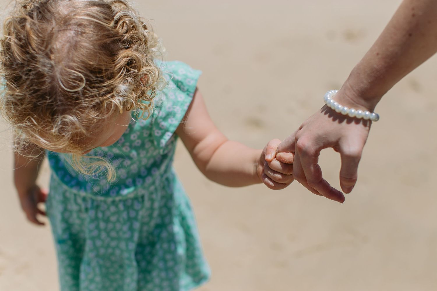 Close-up of mother holding toddler daughter's hand while walking on sandy beach together.