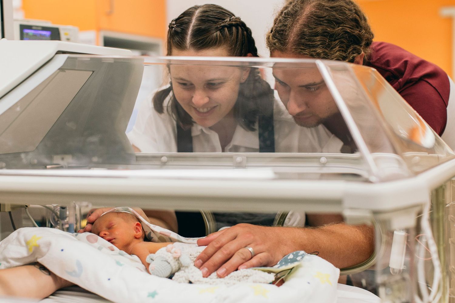 Parents lovingly gaze at their newborn baby in a hospital incubator in the NICU.