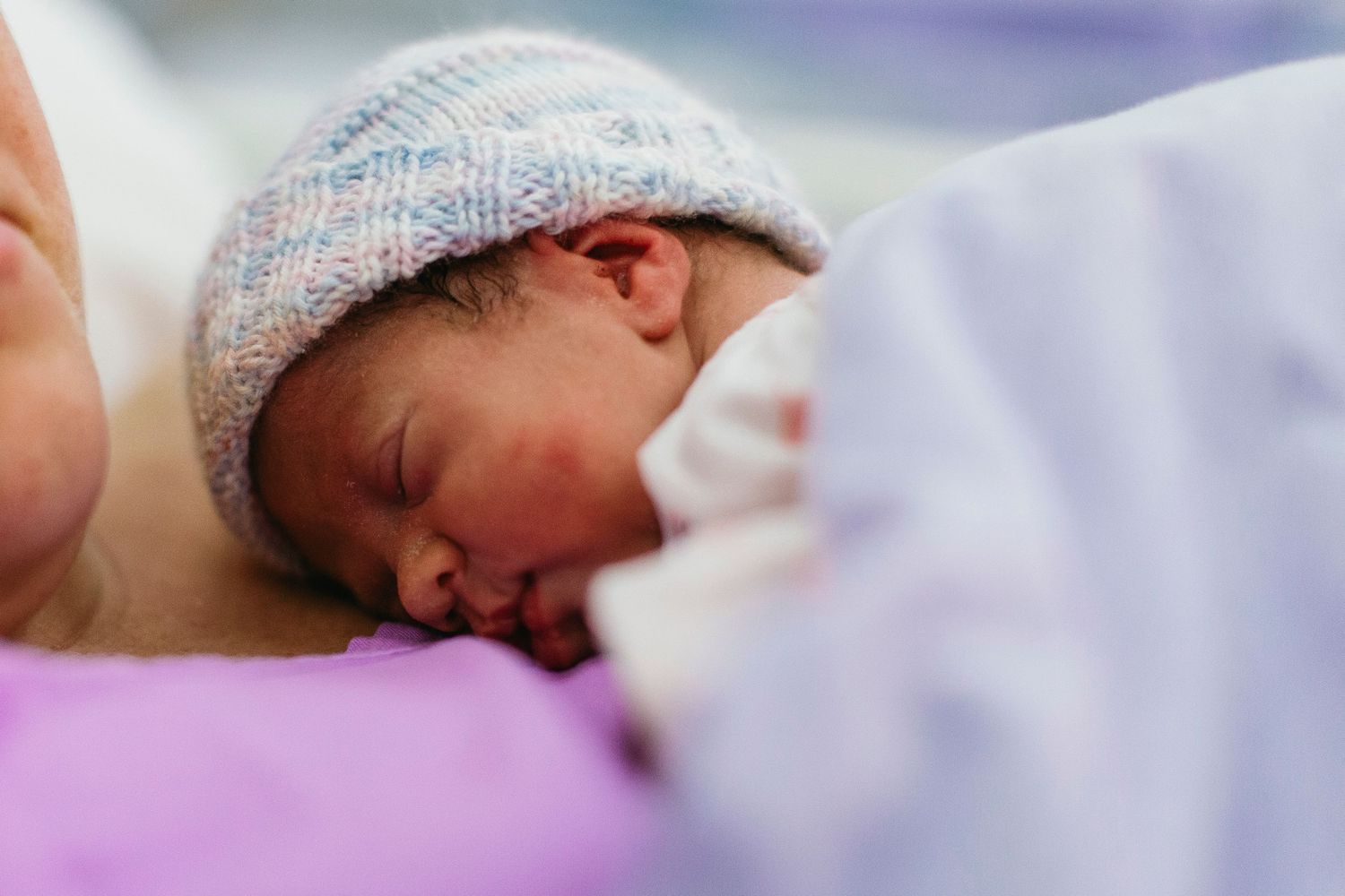 Newborn baby sleeping peacefully wearing a knitted hat, wrapped in soft blankets in a hospital setting.