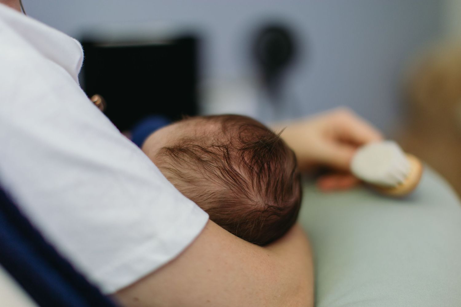Close-up of newborn baby resting on fathers shoulder showing dark hair detail.