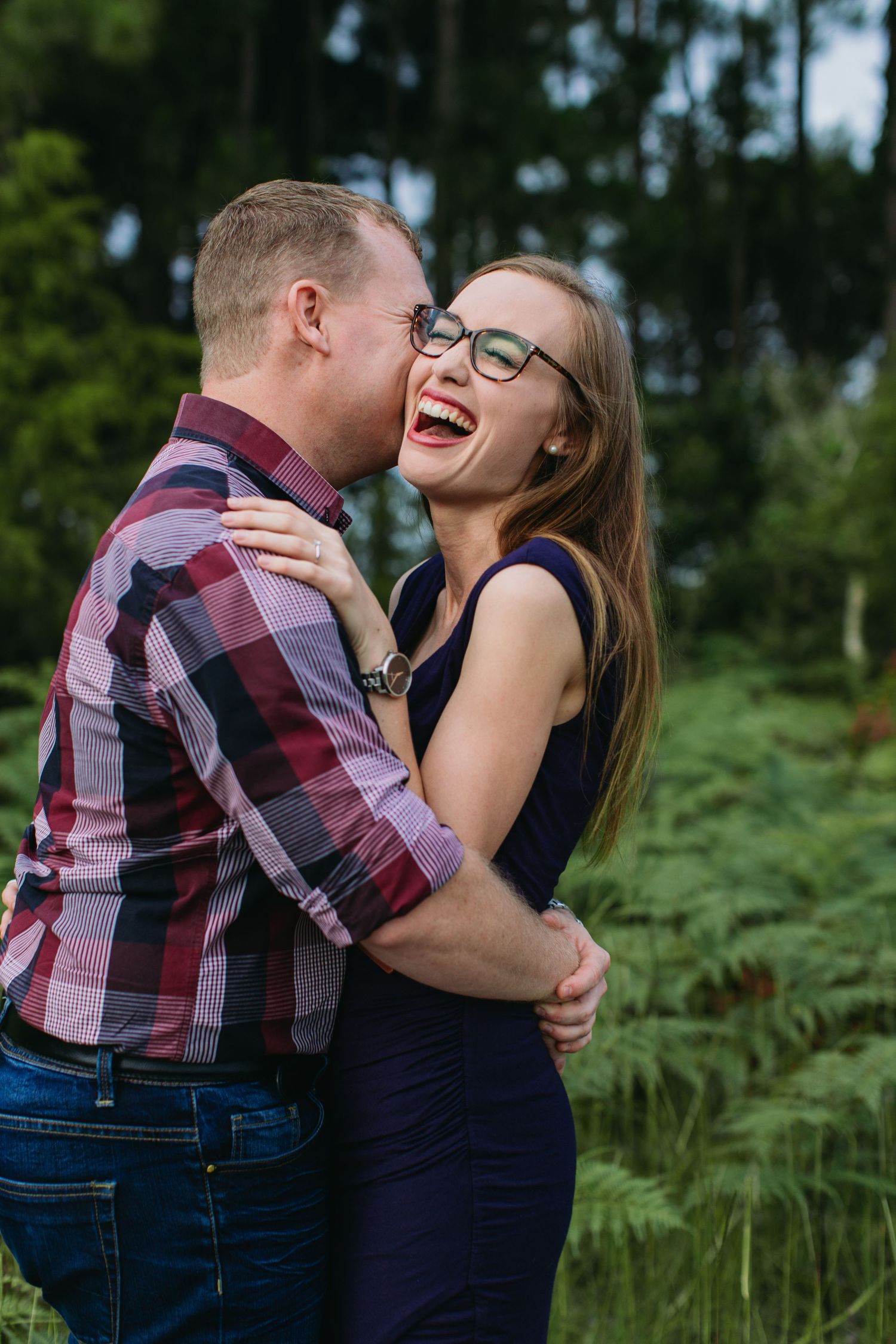 Happy couple embracing and laughing together outdoors in a lush green forest setting.