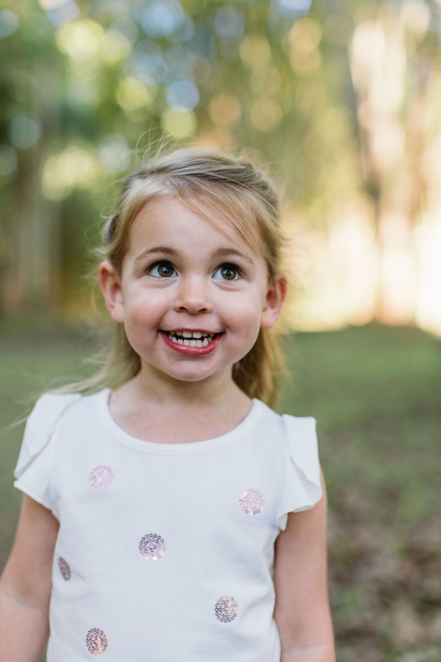 Smiling blonde girl in white sequin dot shirt posing outdoors in natural light.