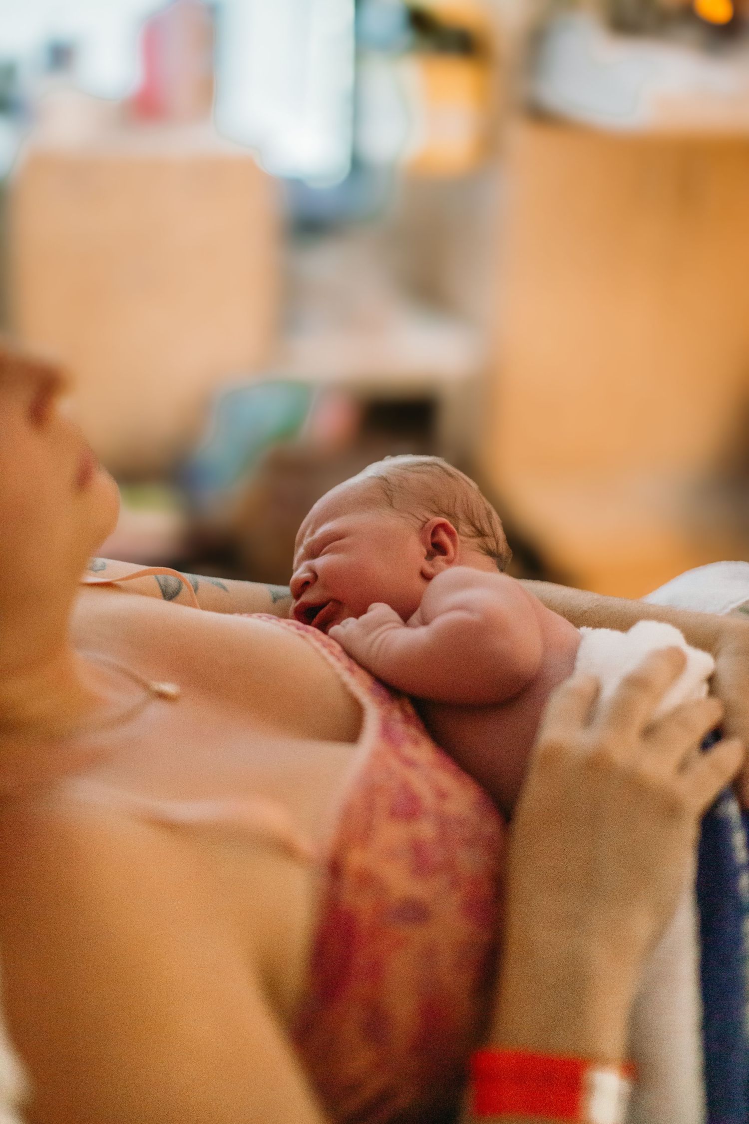 A mother holds her newborn baby skin-to-skin on her chest in a hospital room shortly after birth.