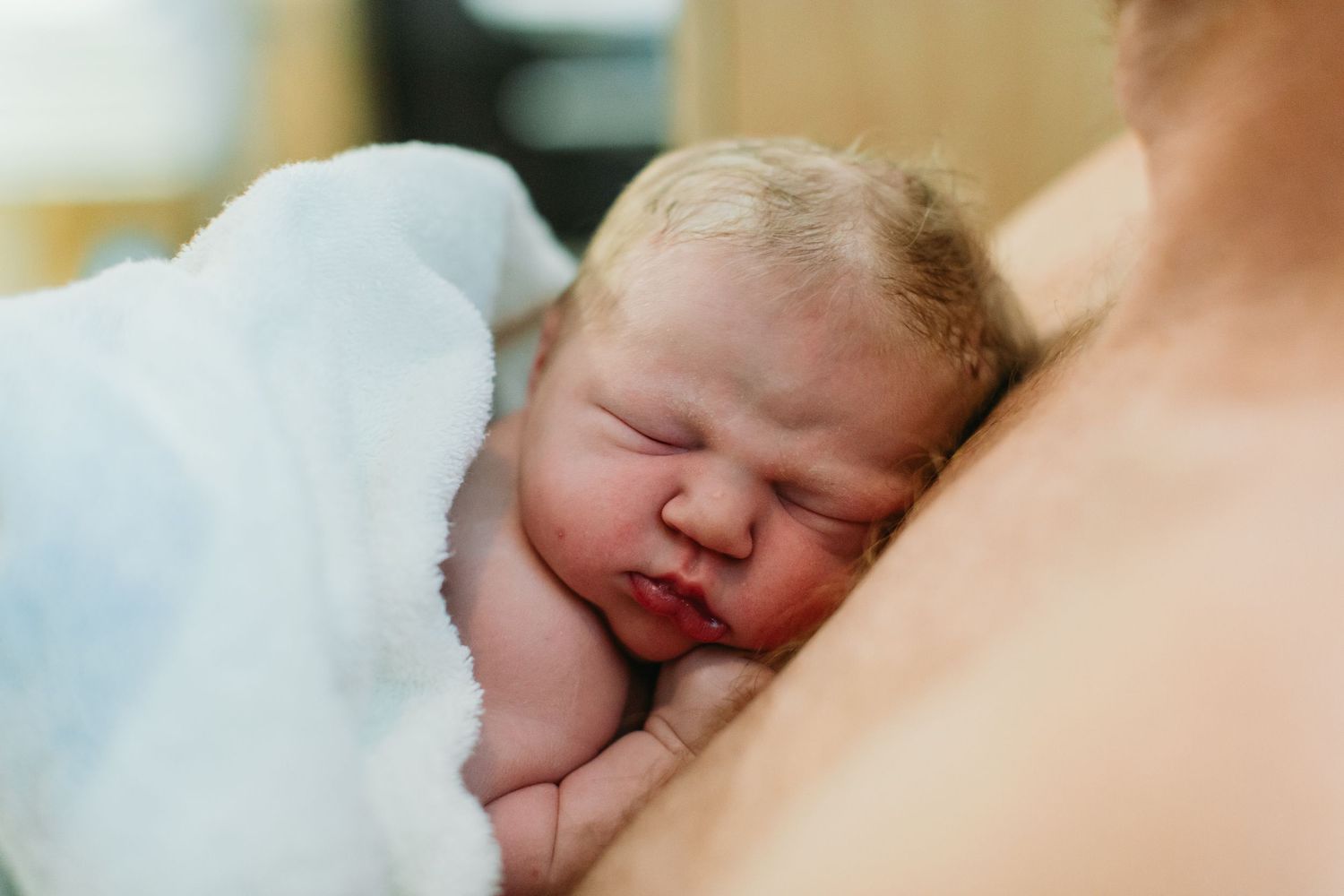 Newborn baby sleeping peacefully on mother's chest wrapped in white blanket after birth.