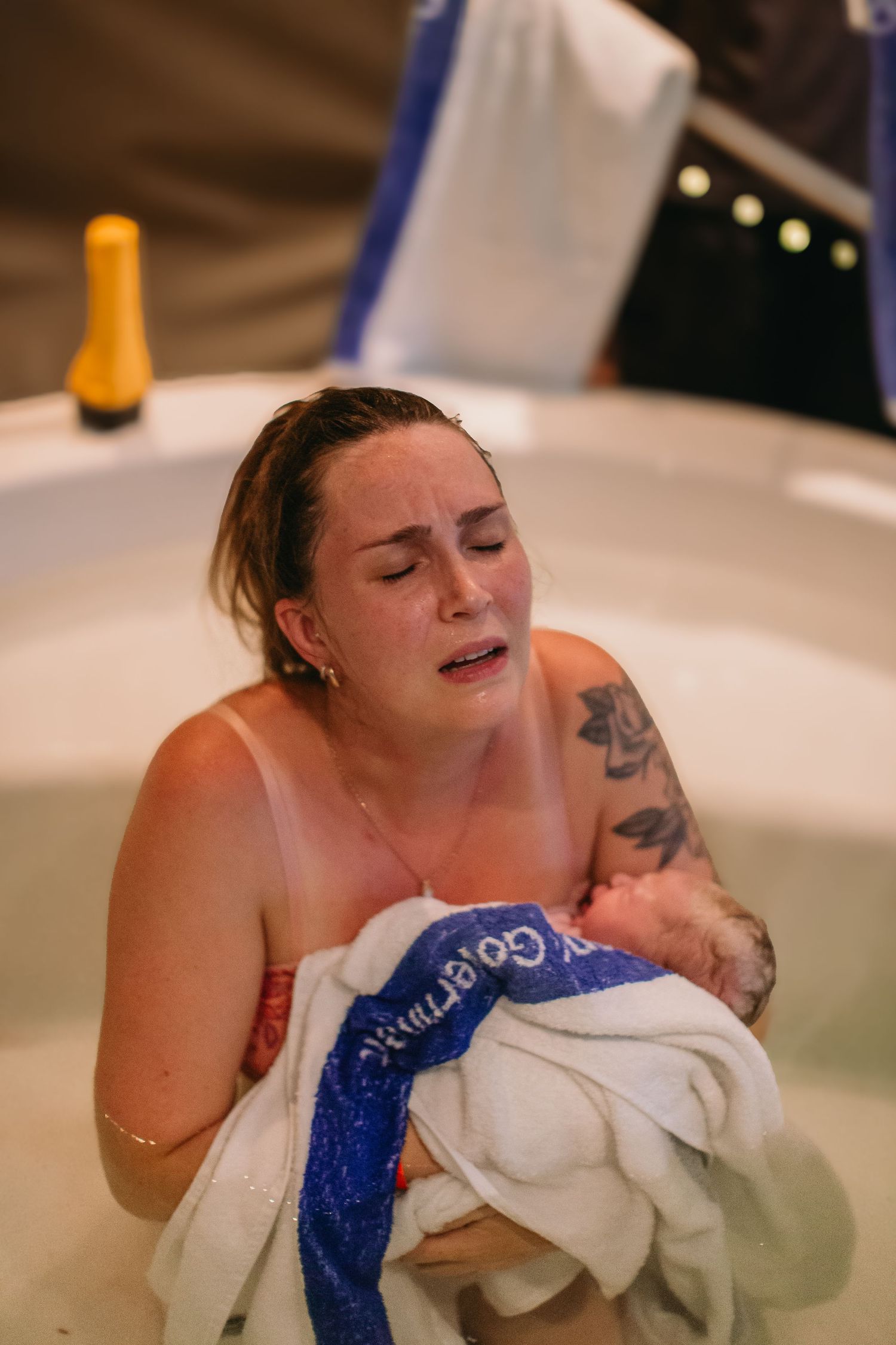 Emotional mother holding newborn baby wrapped in towel during water birth in birthing pool.
