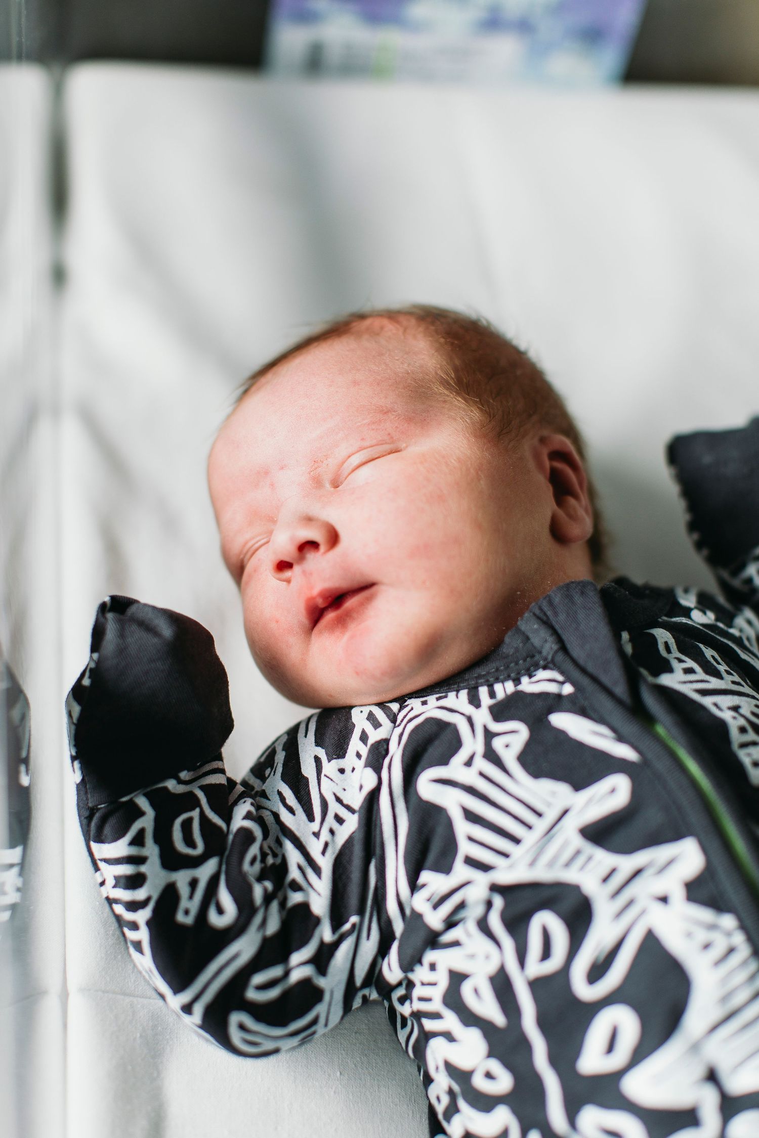 Newborn baby sleeping peacefully in a black and white patterned onesie, lying on a white surface.