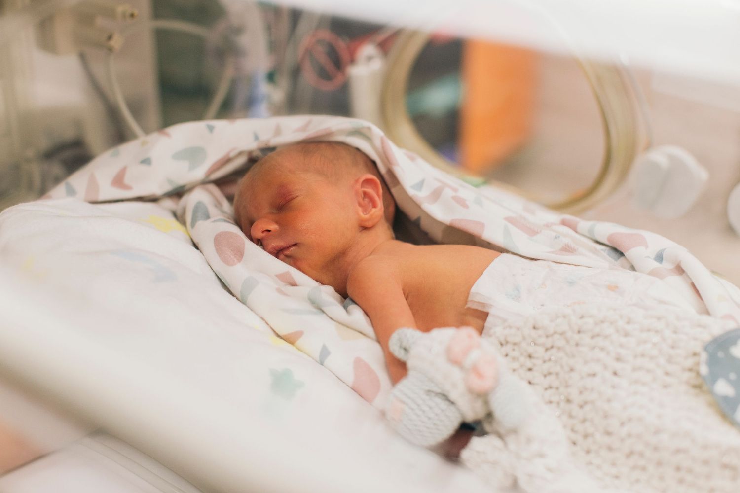Newborn baby sleeping peacefully in a hospital incubator, wrapped in a colorful blanket in the NICU.