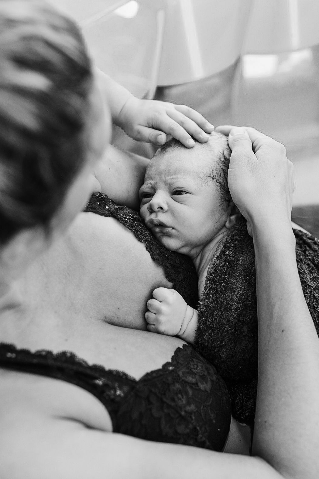 Black and white photo of mother cradling alert newborn baby against chest after birth.