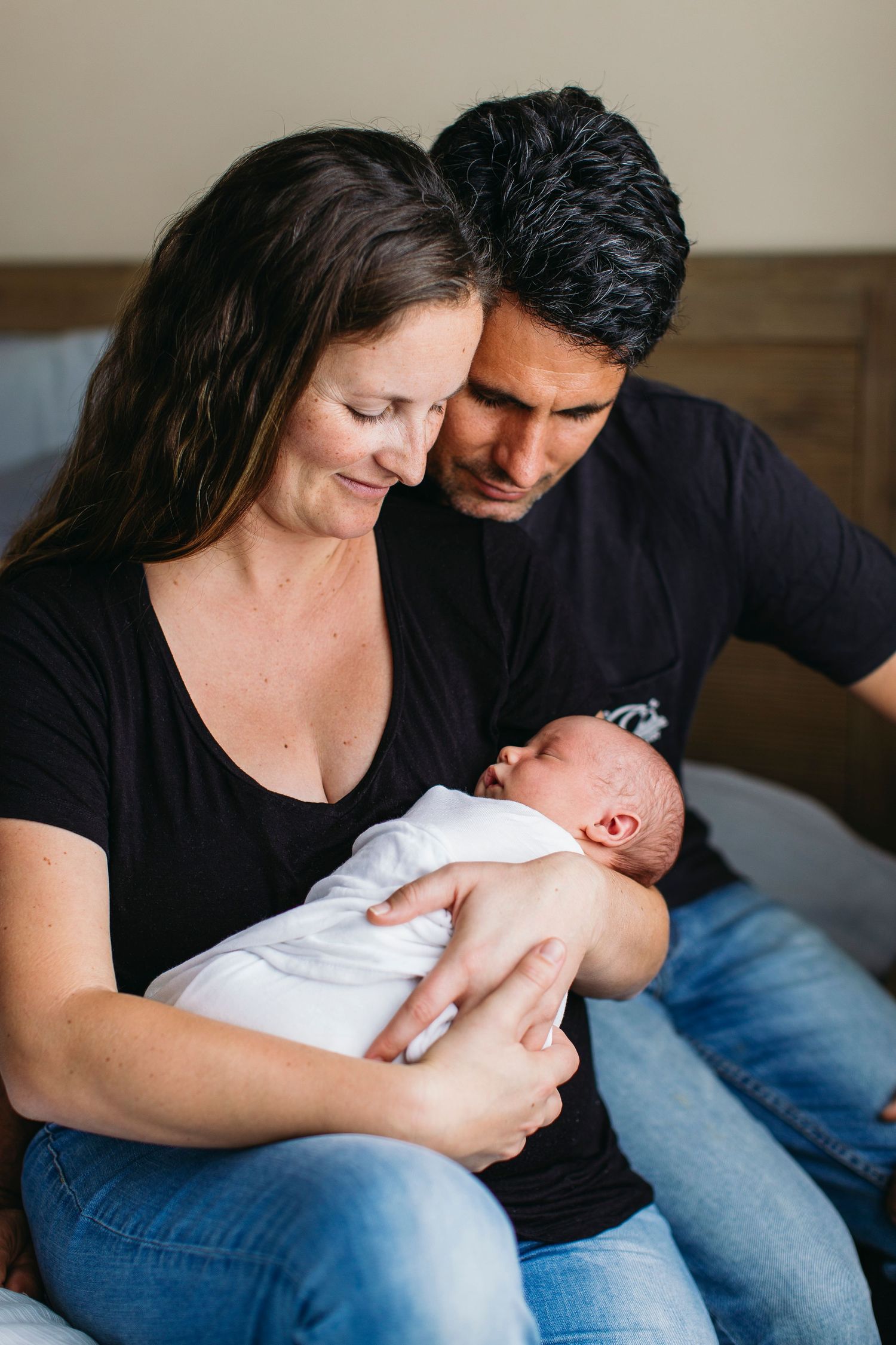 Parents holding their newborn baby while sitting together on the floor, looking down at their infant with love and affection.
