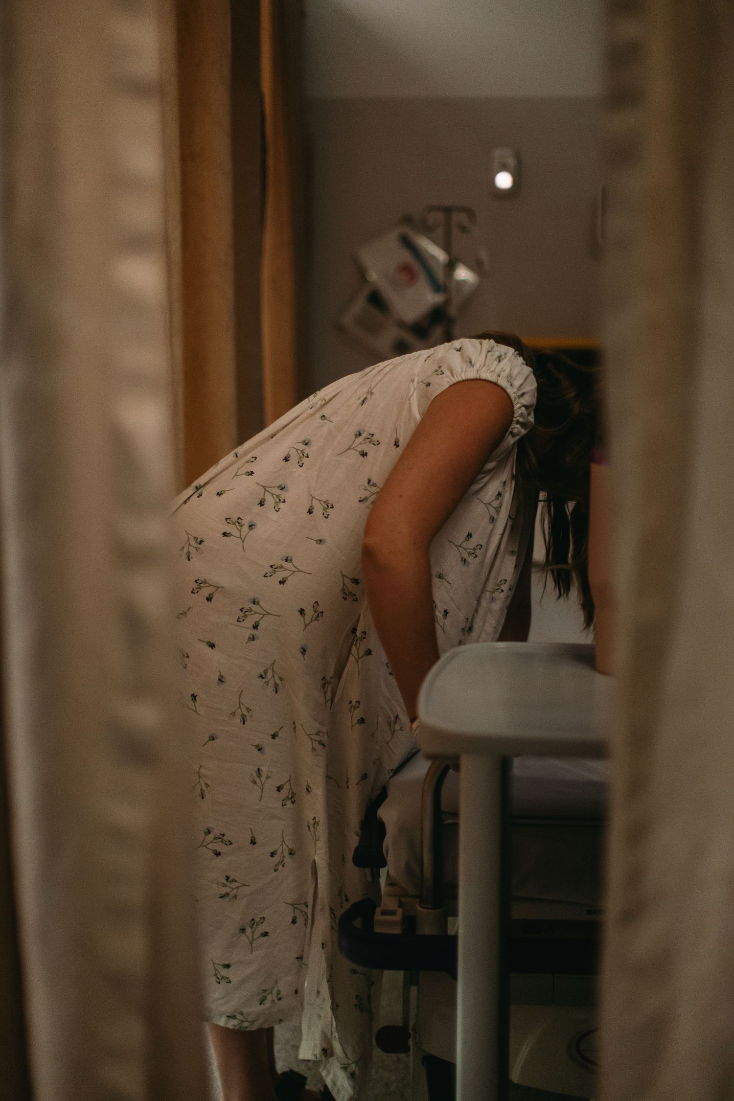 Pregnant woman in floral dress leaning over hospital bed during labor contractions.