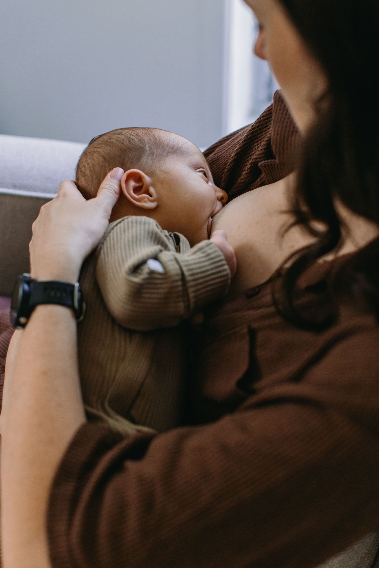 A mother breastfeeding her newborn baby, cradling the infant in her arms while seated comfortably indoors.