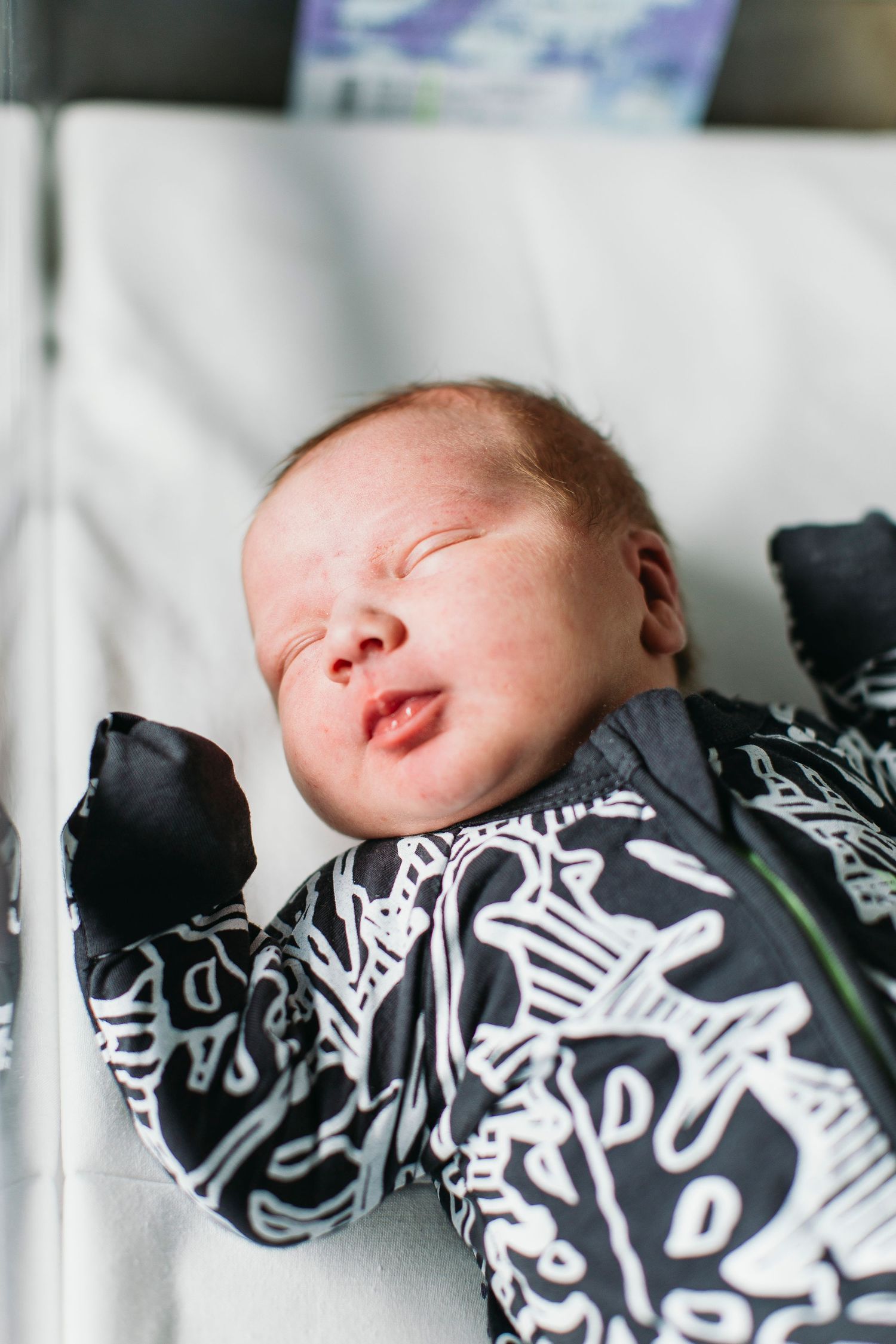 Newborn baby sleeping peacefully in a black and white patterned onesie, lying on a white surface.