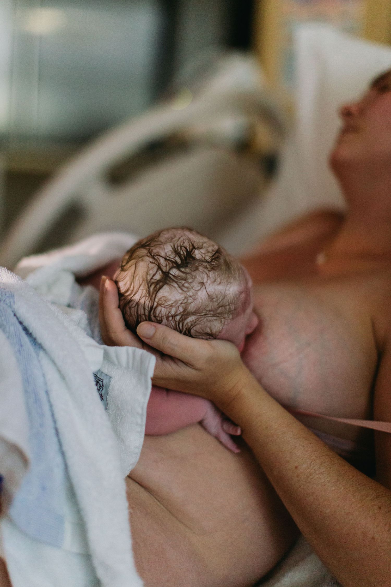Mother holding her newborn baby skin-to-skin in a hospital room after delivery.