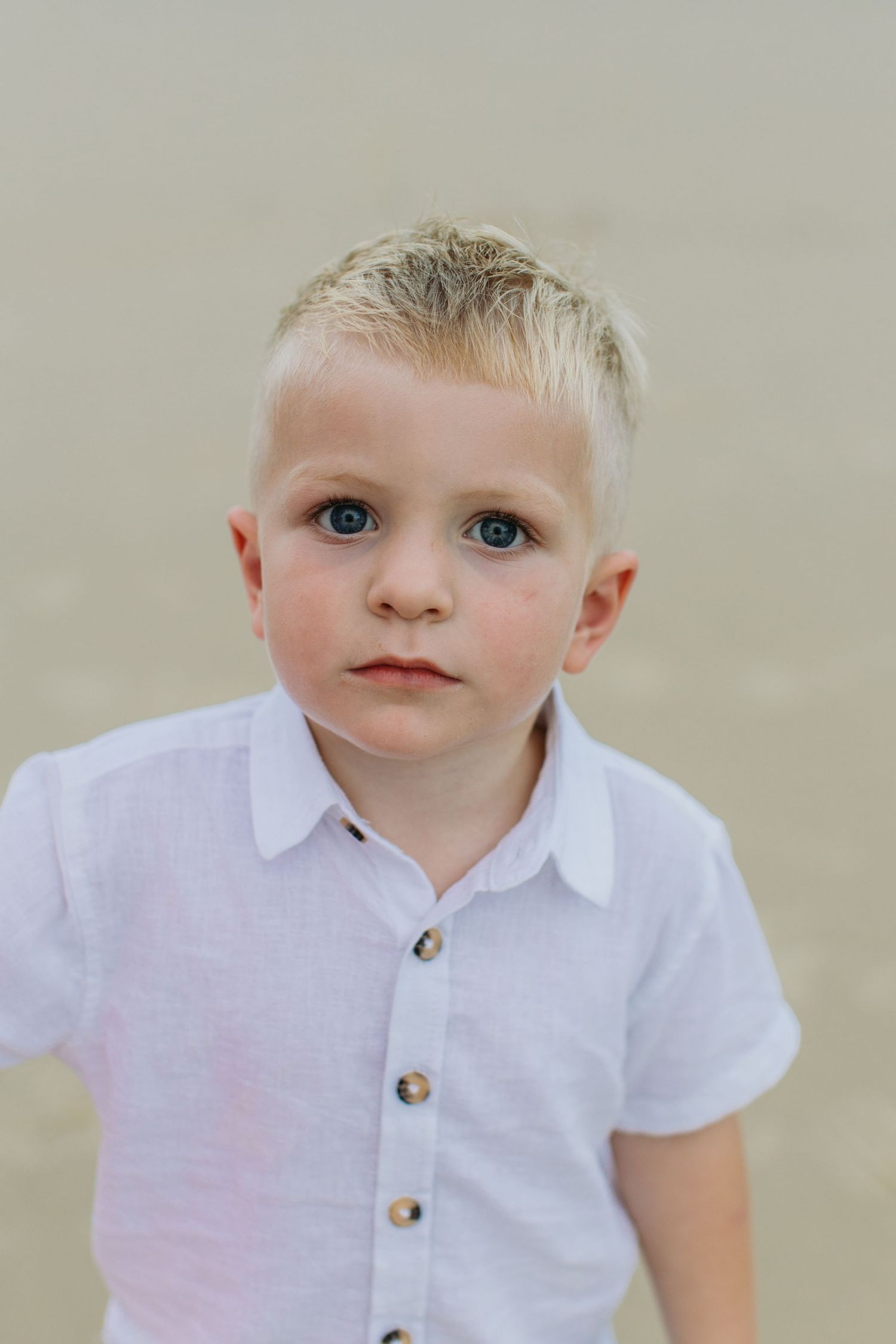 Blonde boy in white linen shirt posing for portrait photo at the beach.