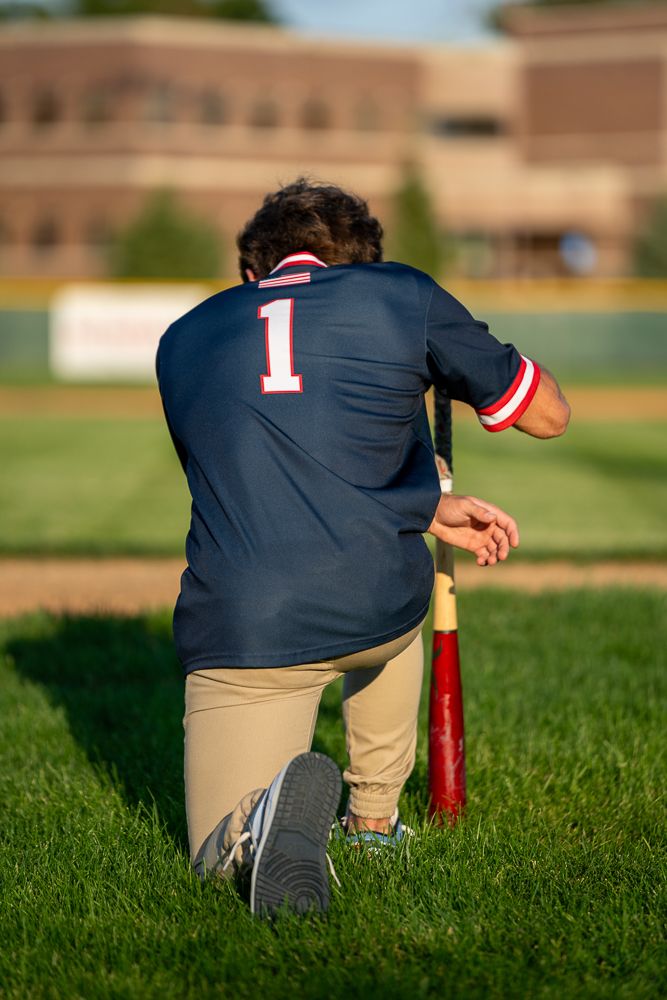 Baseball player wearing number 1 jersey kneeling on grass field, leaning on bat during game.
