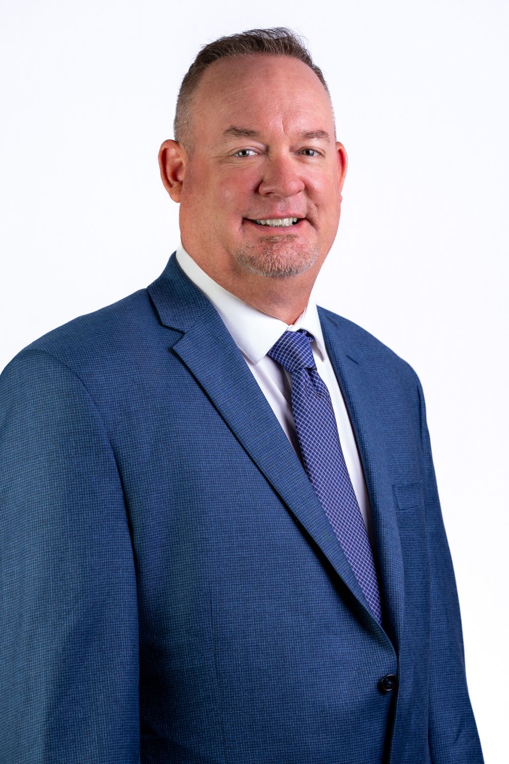 Professional man in blue suit and tie smiling confidently against white background.