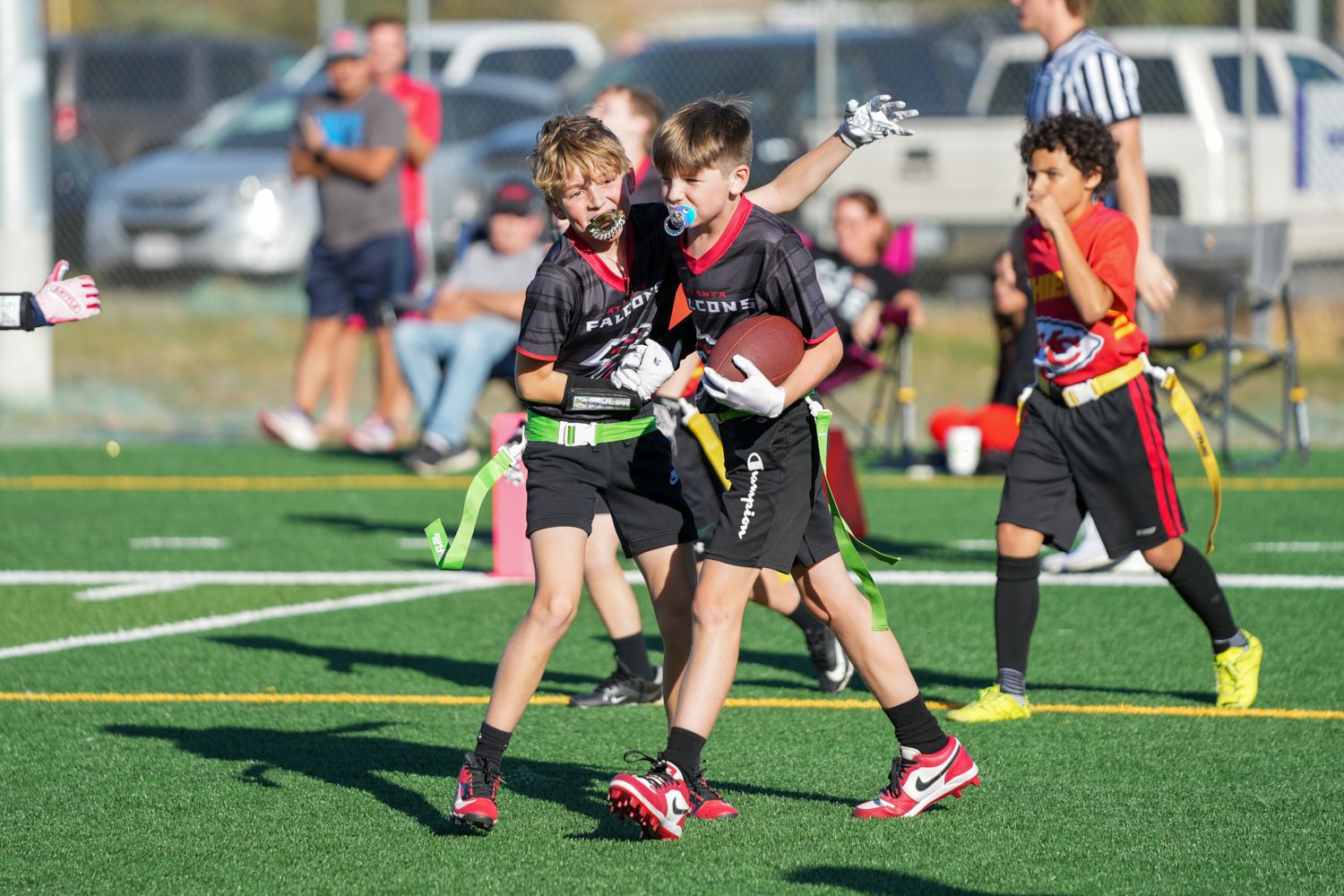 Youth flag football players celebrating on green turf field during daytime game.