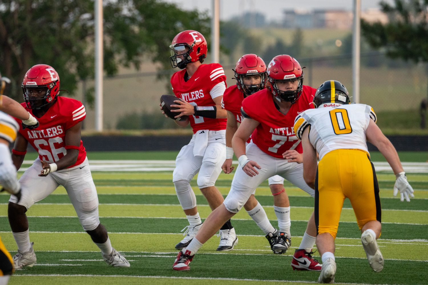 Red-uniformed Antlers quarterback drops back to pass behind offensive linemen during a high school football game.