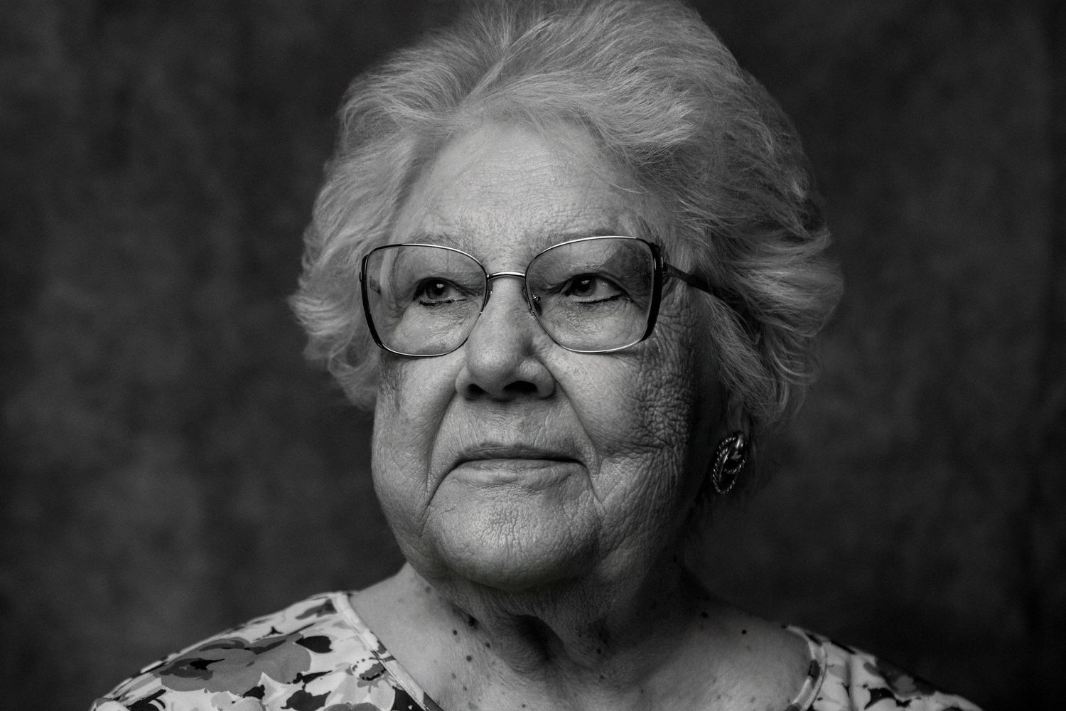 Black and white portrait of an elderly woman with glasses looking at camera.