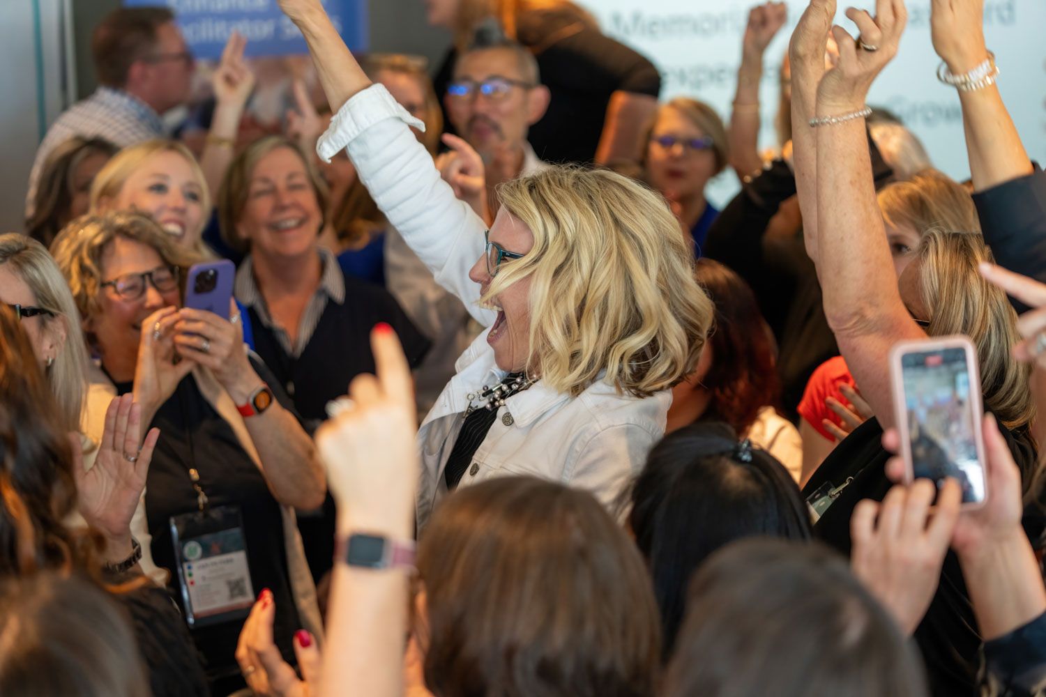 Excited crowd of women celebrating with raised hands at a conference event.