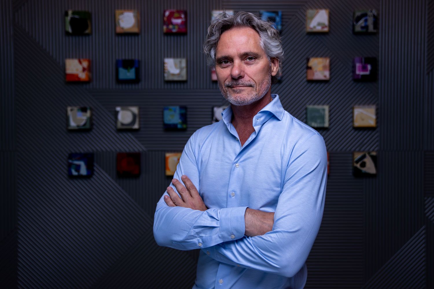 Confident businessman with gray hair standing with arms crossed in a modern office with colorful wall art.