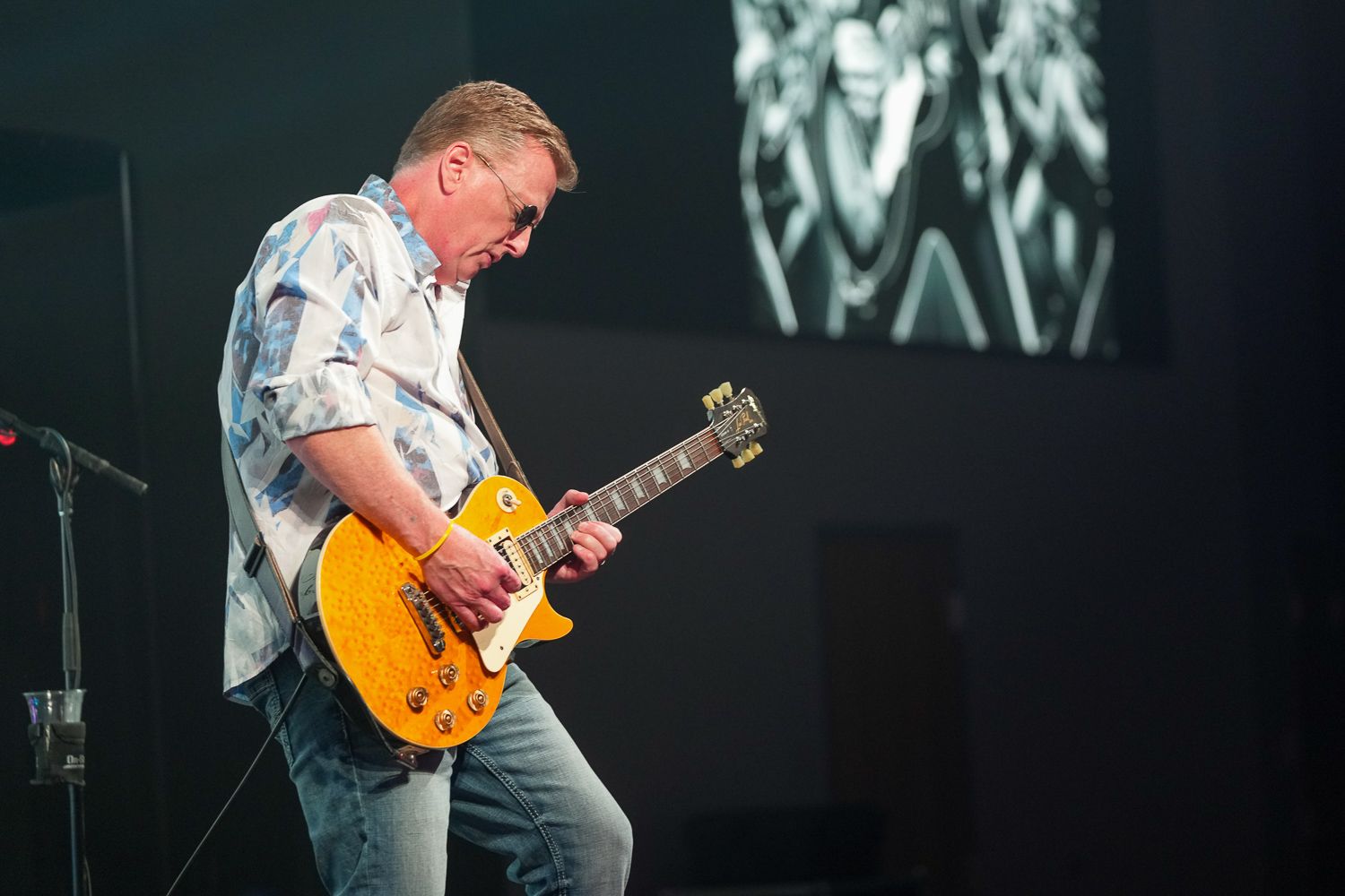 Guitarist performing on stage playing a Les Paul electric guitar under dramatic lighting.