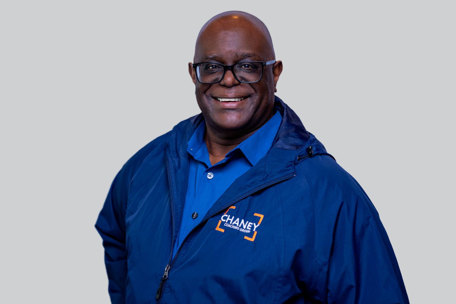 Smiling man wearing a blue Chaney branded jacket against a gray background.