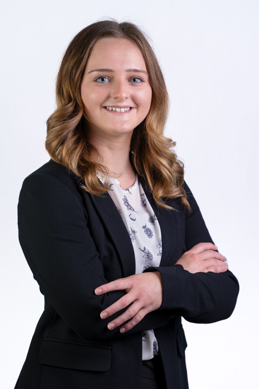 Young professional woman in black blazer smiling with arms crossed against white background.