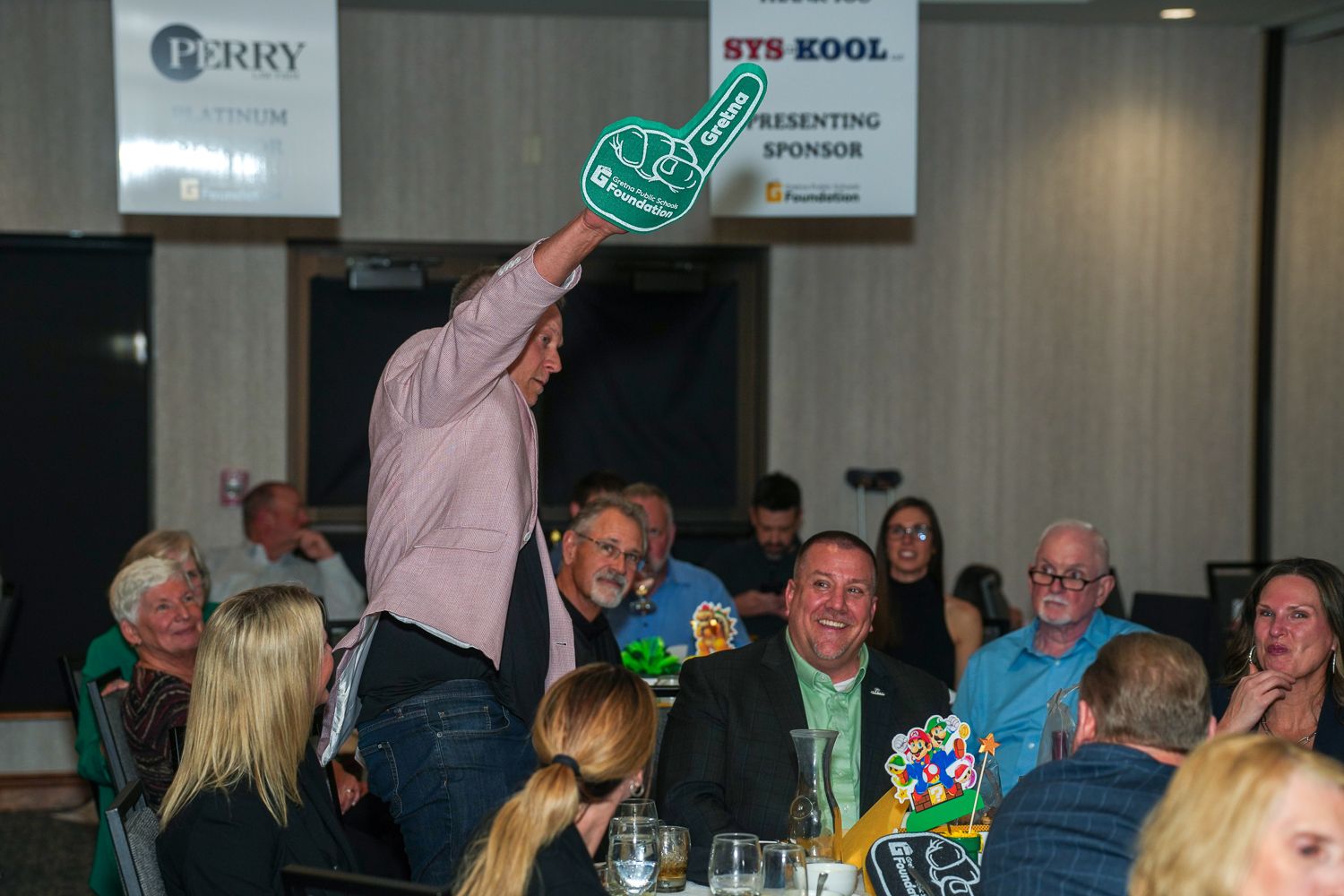 Excited man holding a large foam finger at a crowded event with STS-KOOL presenting sponsor banner.