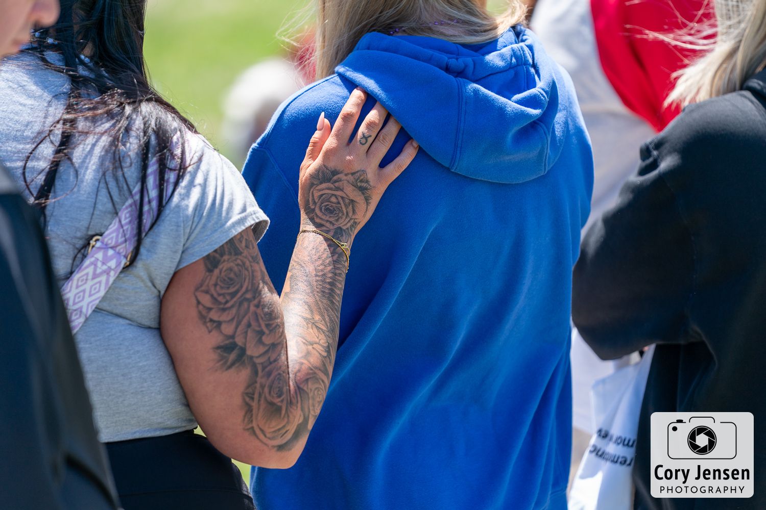Close-up of a person with detailed rose tattoos on their arm at an outdoor gathering.