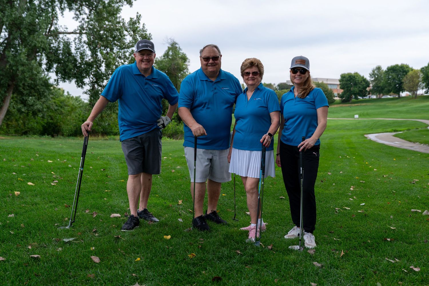 Four golfers in matching blue shirts pose together smiling on a golf course fairway.