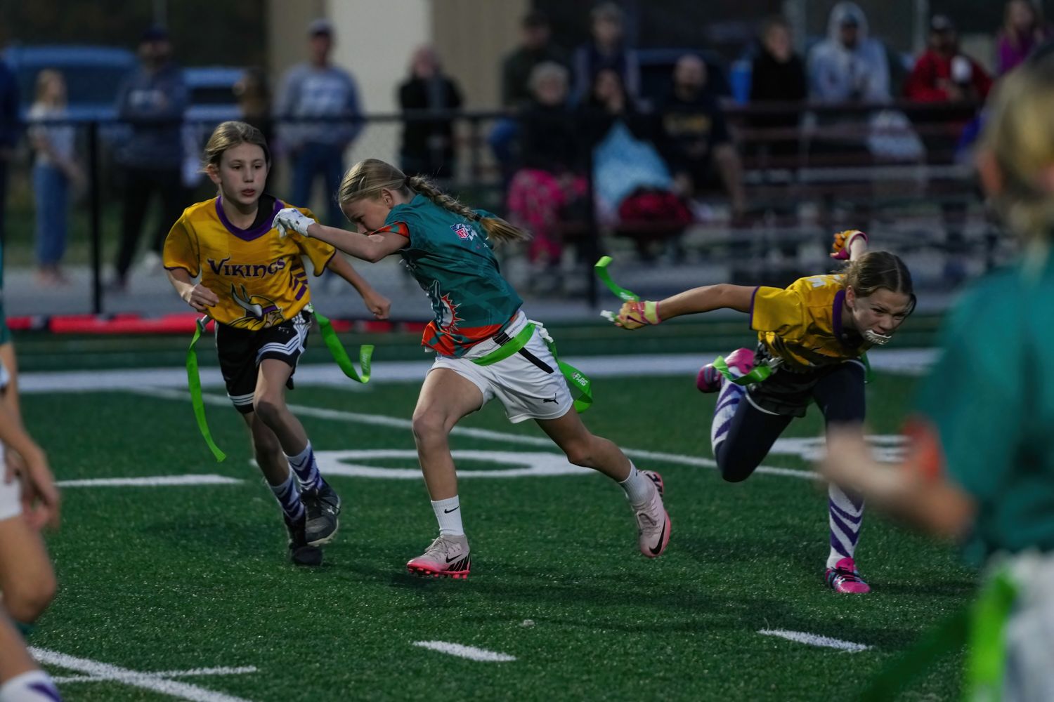 Young female flag football players competing on turf field during evening game.