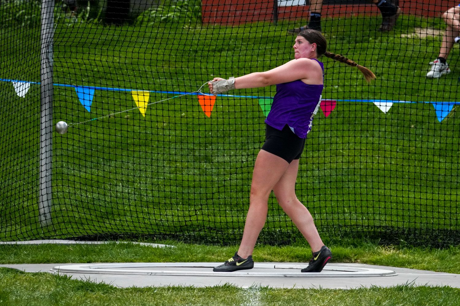 Female athlete in purple uniform spinning to throw a hammer at an outdoor track and field competition.