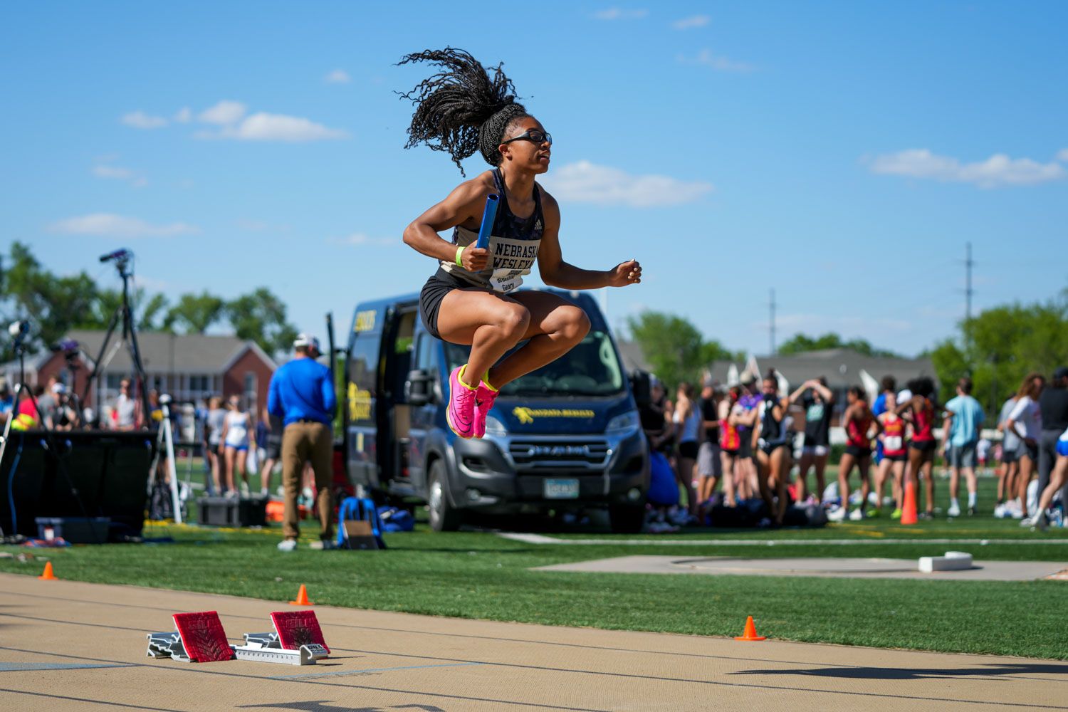 Female athlete mid-air warming up for a race at an outdoor track and field competition on a sunny day.