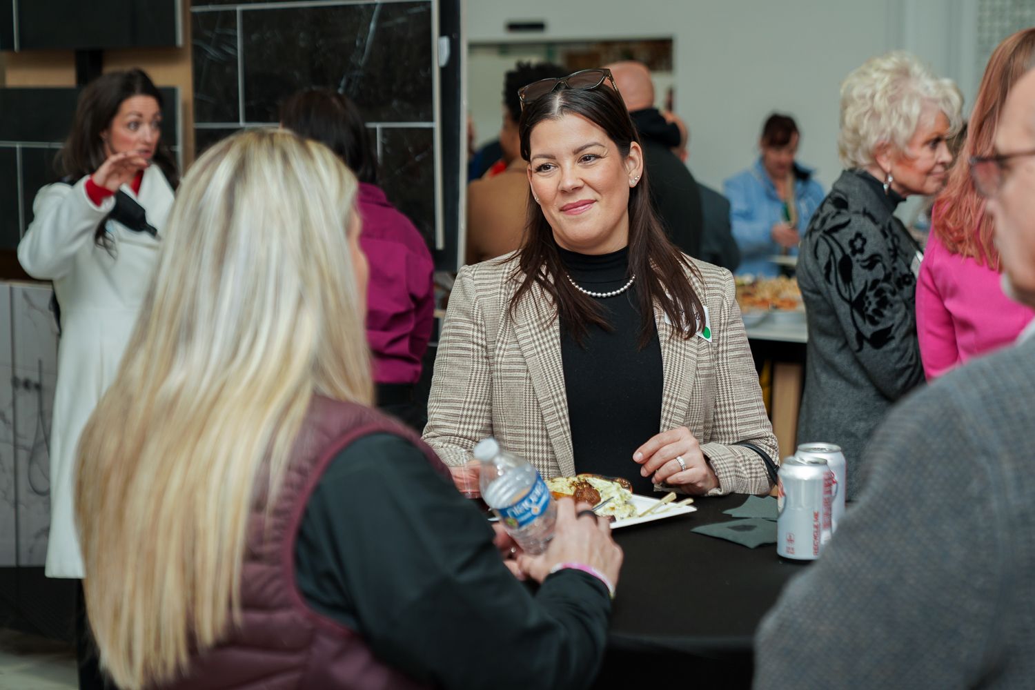 Woman in plaid blazer smiling and conversing with others at a casual networking event.