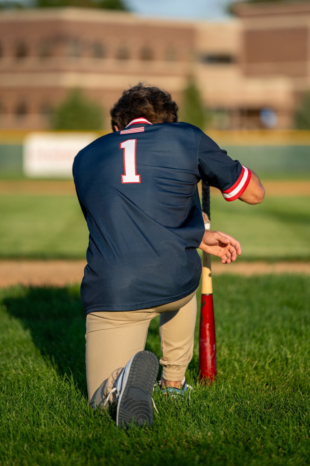 Baseball player wearing number 1 jersey kneeling on green field holding a bat during a game.
