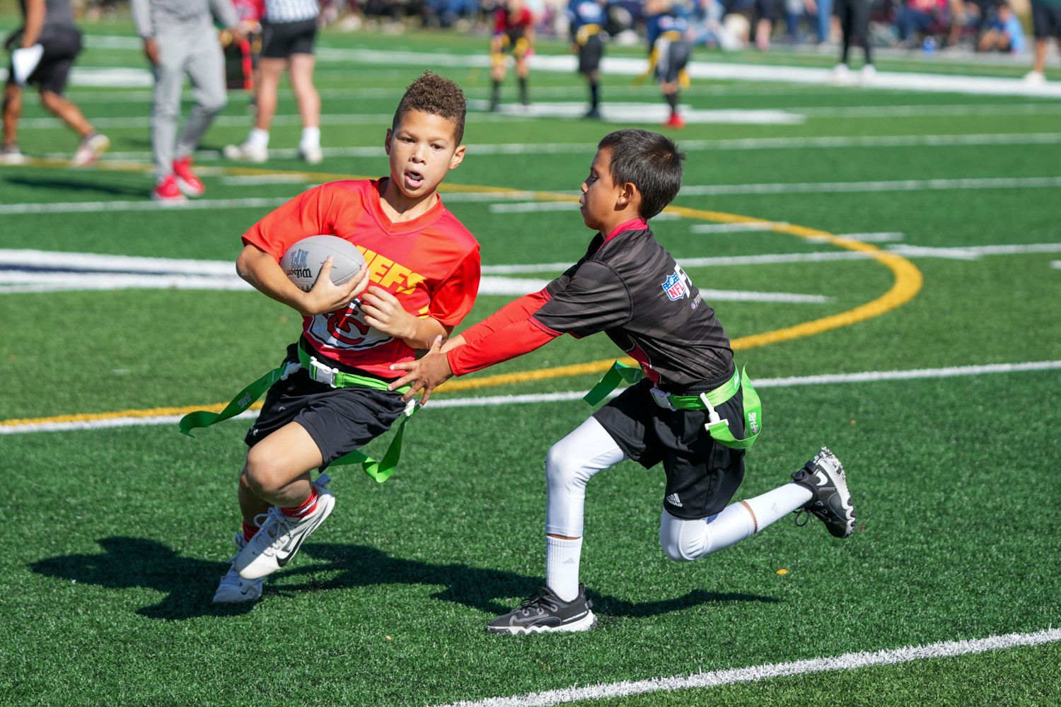 Two young boys competing in flag football game on green turf field outdoors.