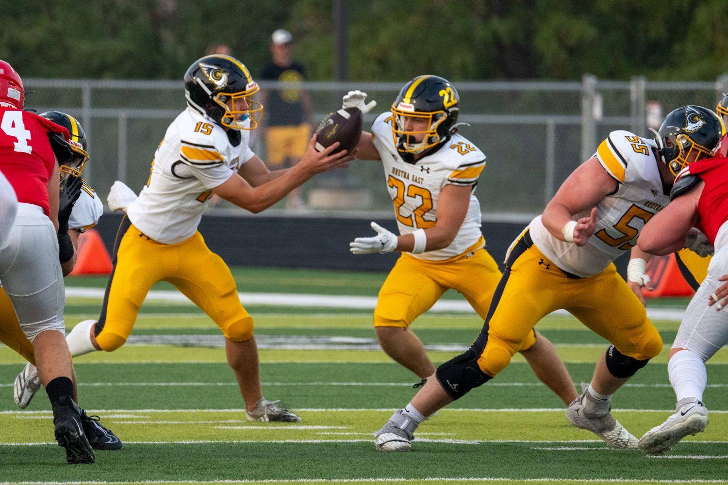 High school football players in gold uniforms executing handoff play during game.