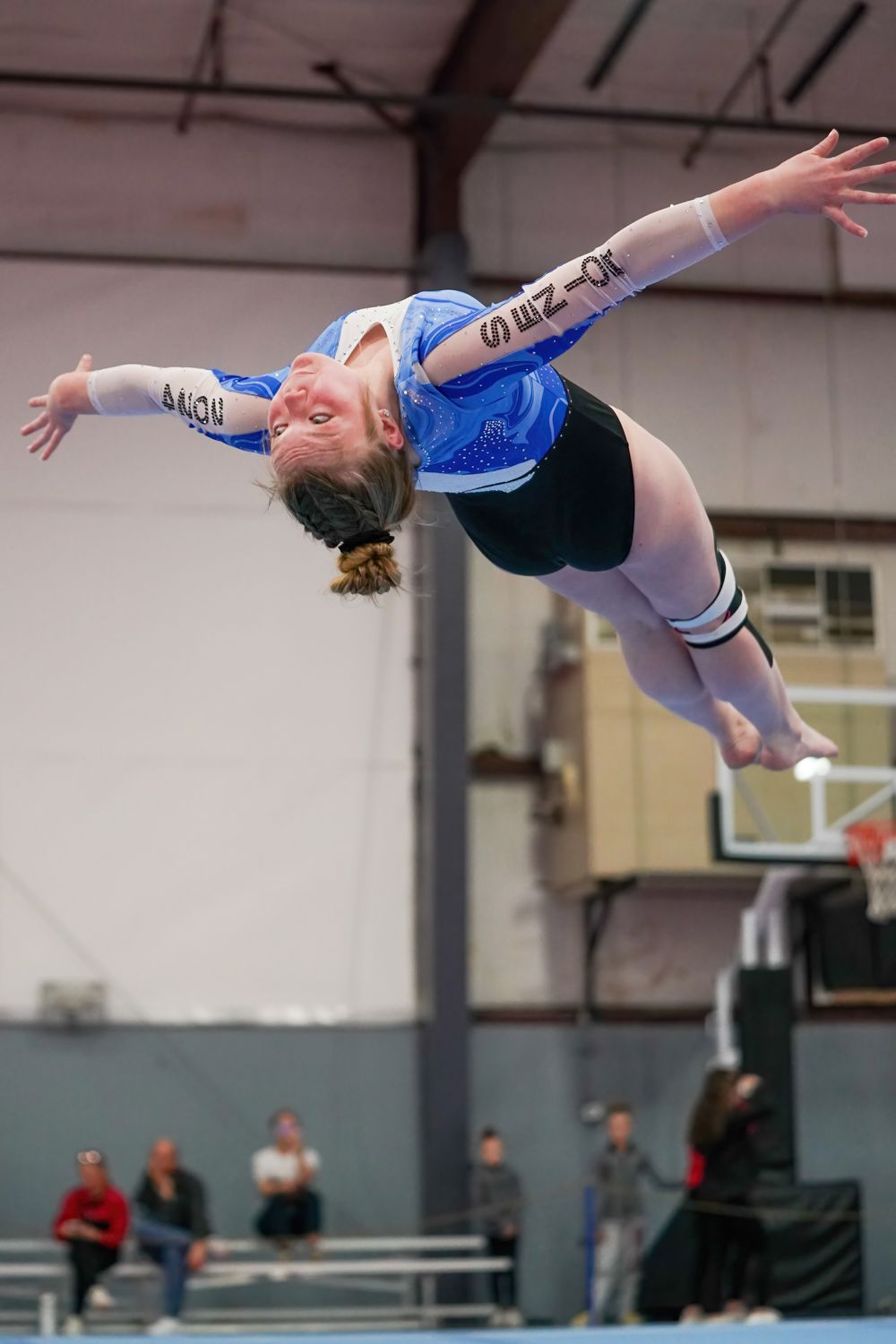 Young female gymnast performing a back flip on a balance beam during an indoor gymnastics competition.