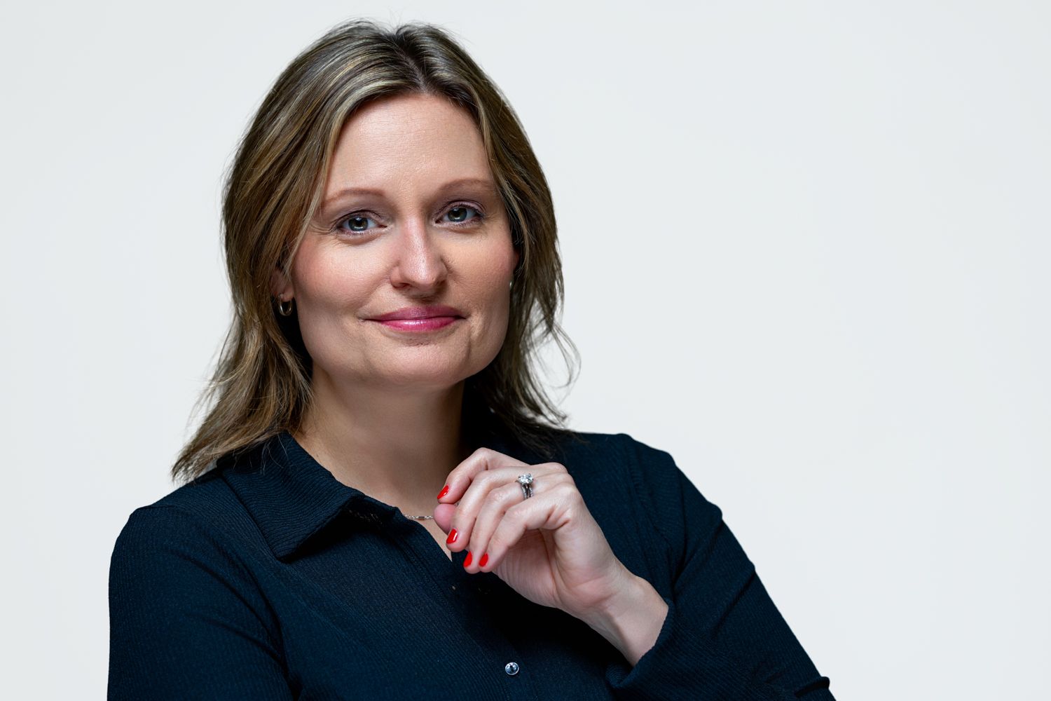 Professional woman in black blouse smiling with hands clasped against a clean white background.