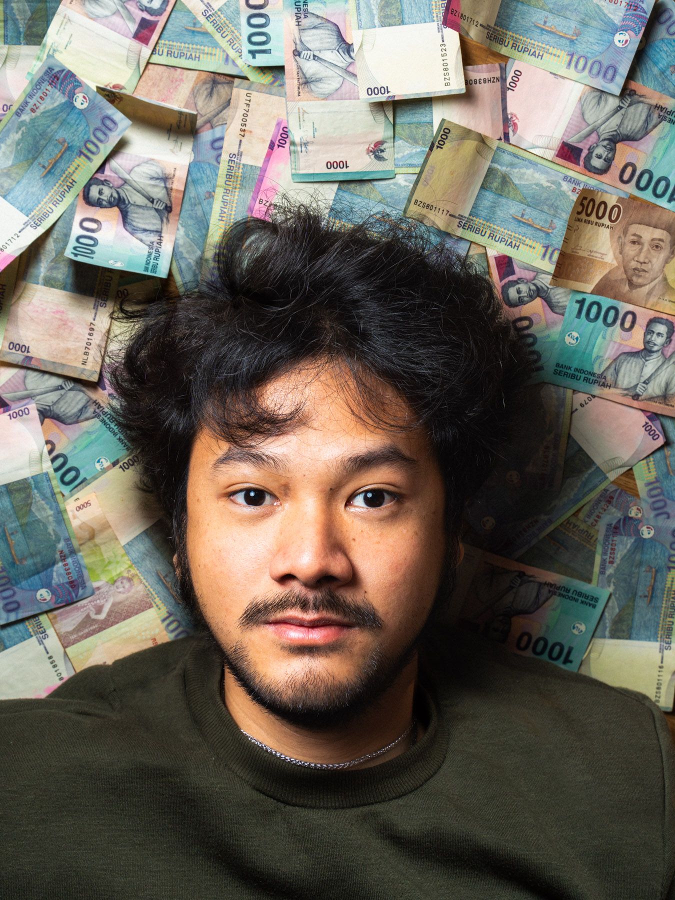 Portrait von Nico, Student aus Indonesien und Barista, auf indonesischen Geldscheinen liegend