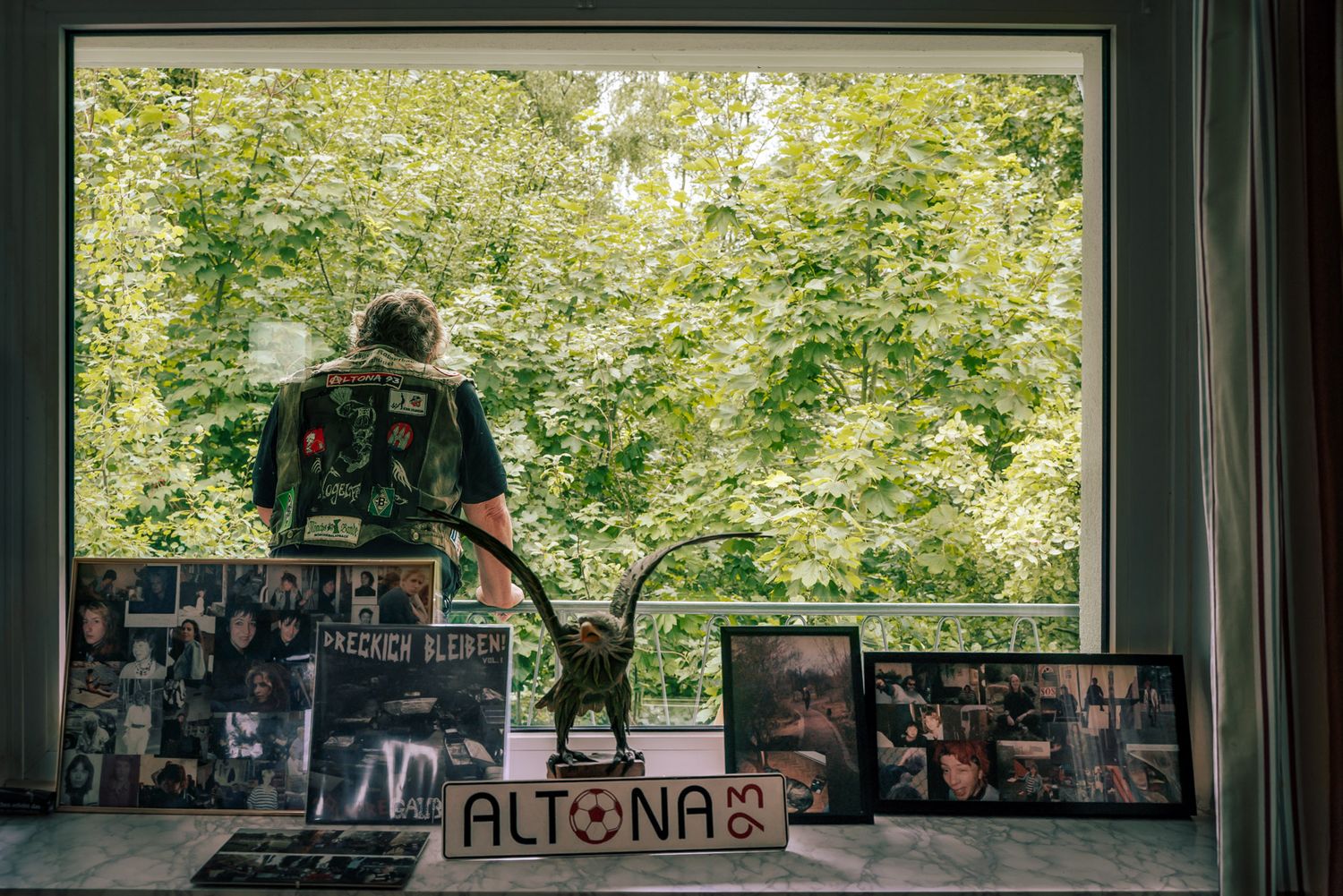 Blick auf die Fensterbank mit gerahmten Bildern und Torsten Herrmann auf dem Balkon dahinter mit Blick ins Grüne